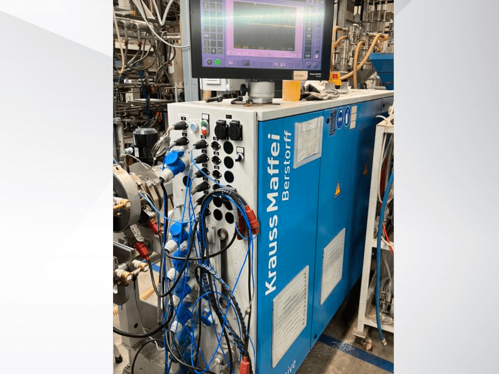 Krauss Maffei Berstorff industriālā mašīna ar vadības paneli un monitoru, ar dažādām pogām un pievienotām šļūtenēm, skats no sāniem.