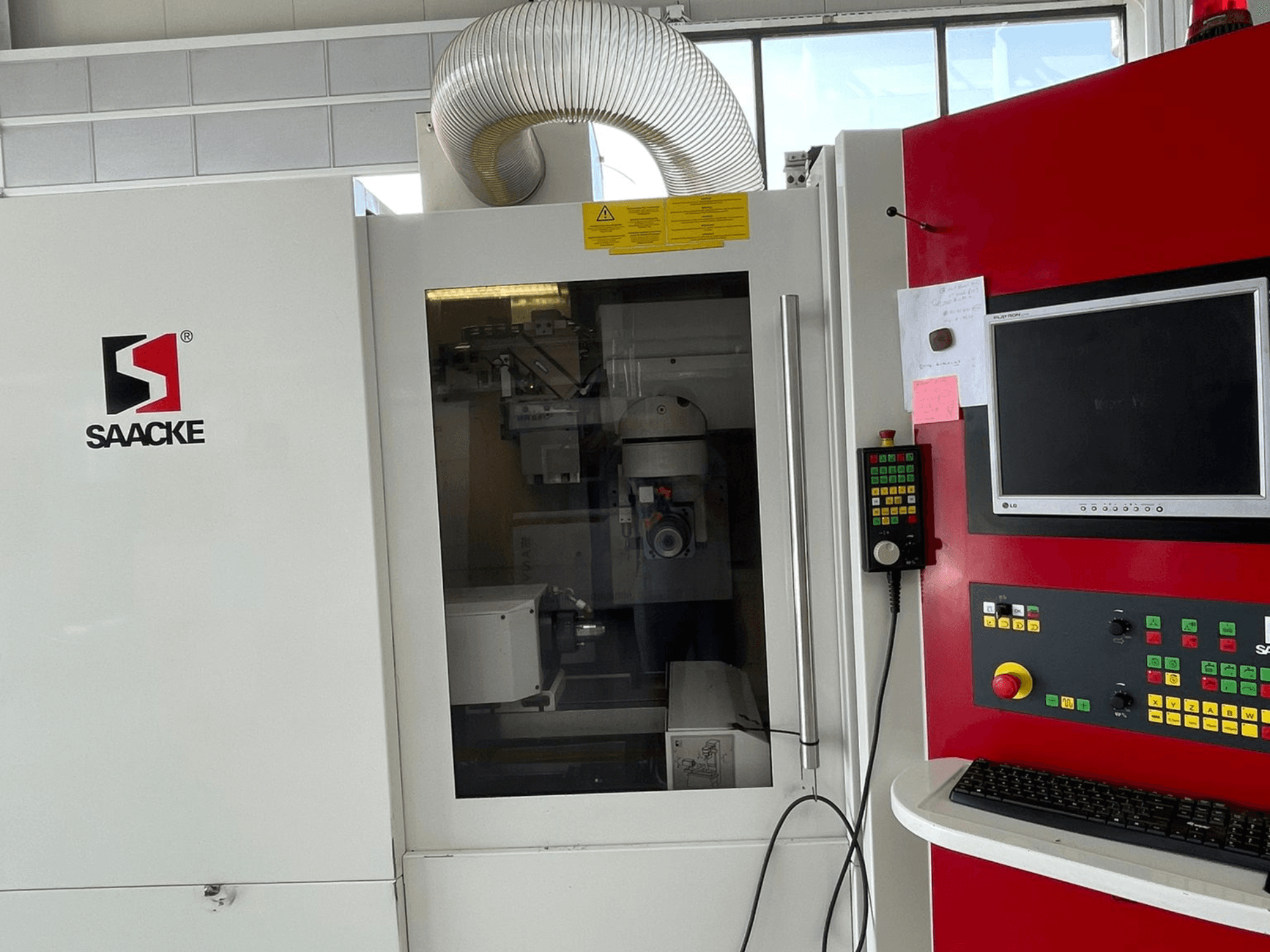 SAACKE mašīna baltā un sarkanā krāsā, skats no priekšpuses, ar vadības paneli, monitoru un caur stiklu redzamām iekšējām daļām.
