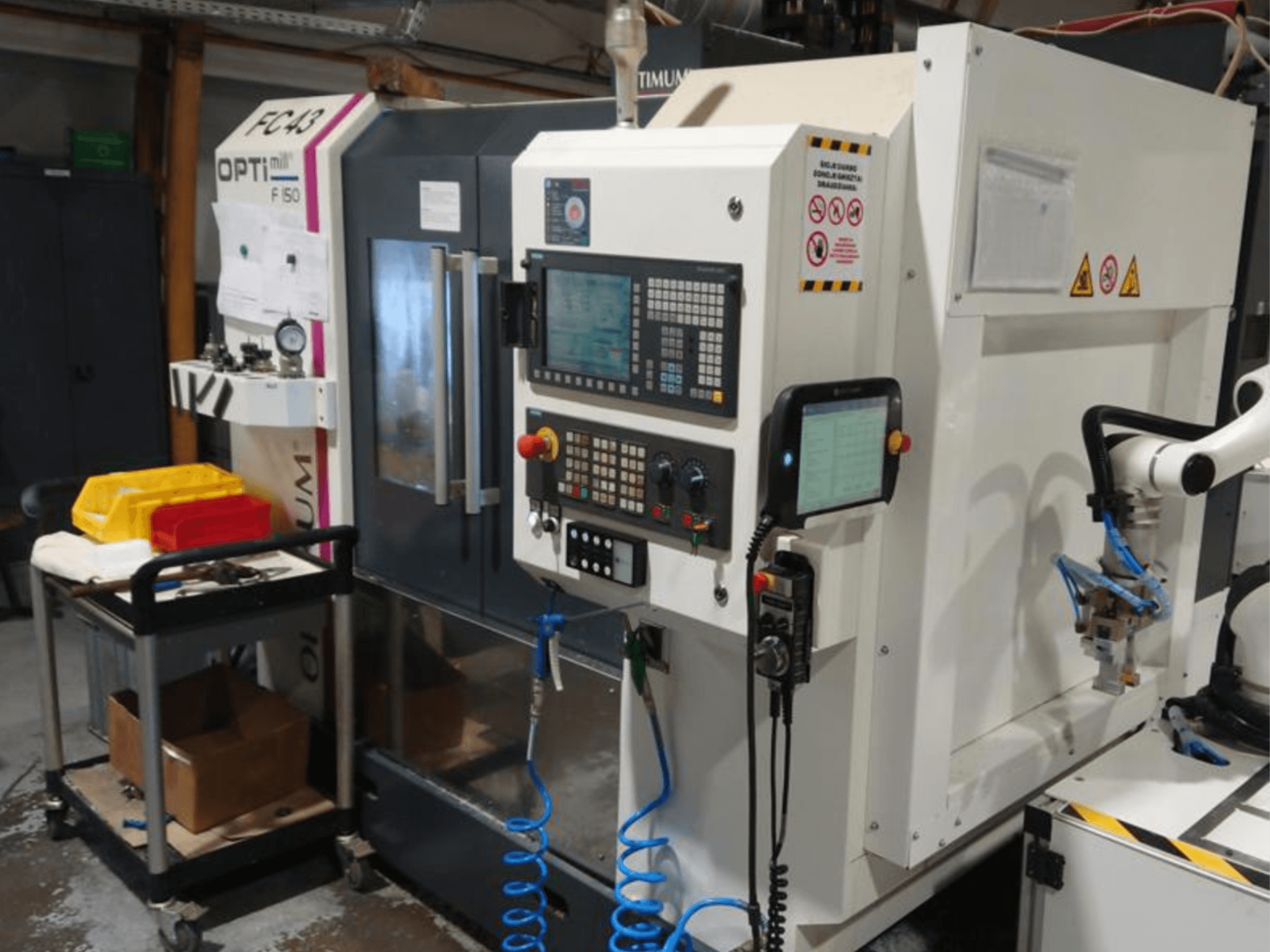 OPTIMUM F50 frēzmašīnas vadības panelis ar šļūtenēm, instrumentiem un robota roku darbnīcā.