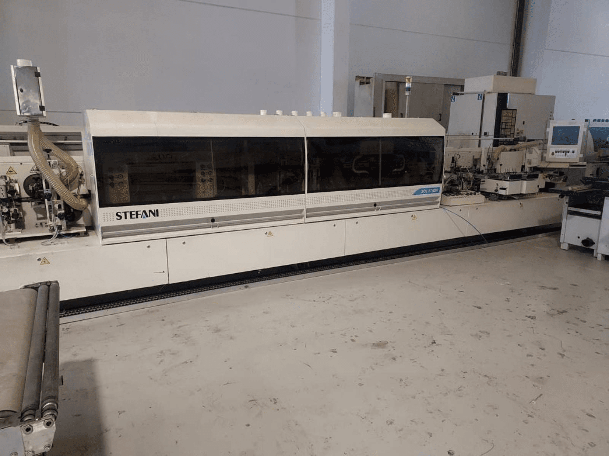 Stefani Solutions malu aplīmēšanas iekārta, skats no priekšpuses, ar redzamu putekļu nosūces sistēmu un vadības paneli, darbnīcā.