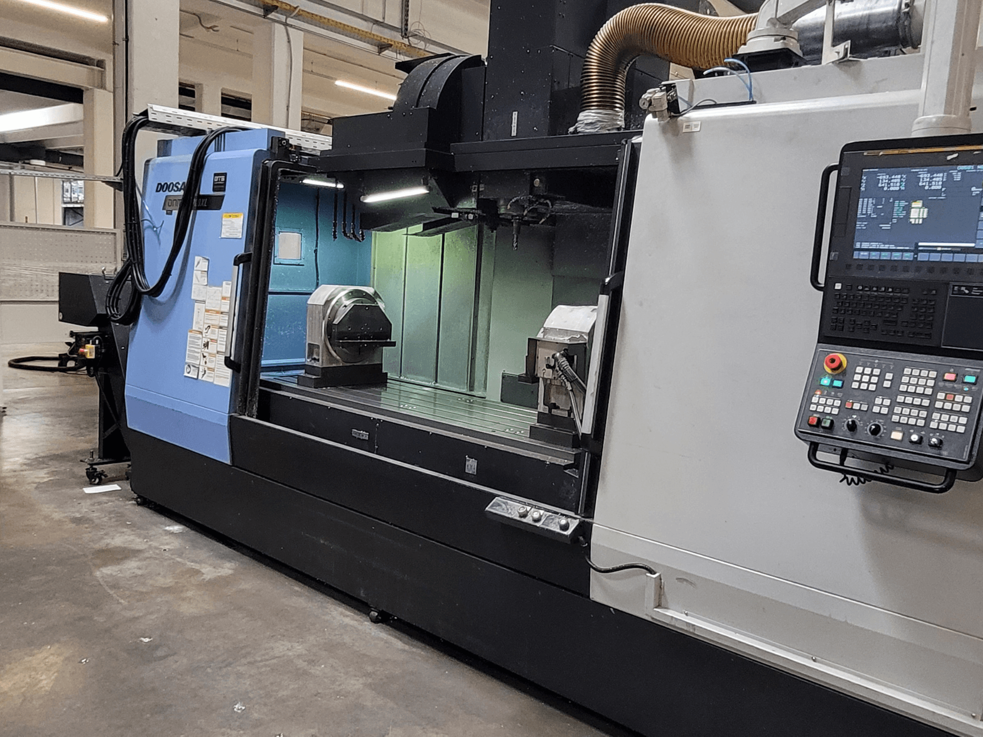 Vertikālais apstrādes centrs DOOSAN DNM 6700 XL, skats no priekšpuses, kurā redzams vadības panelis, darba galds un apstrādes zona.