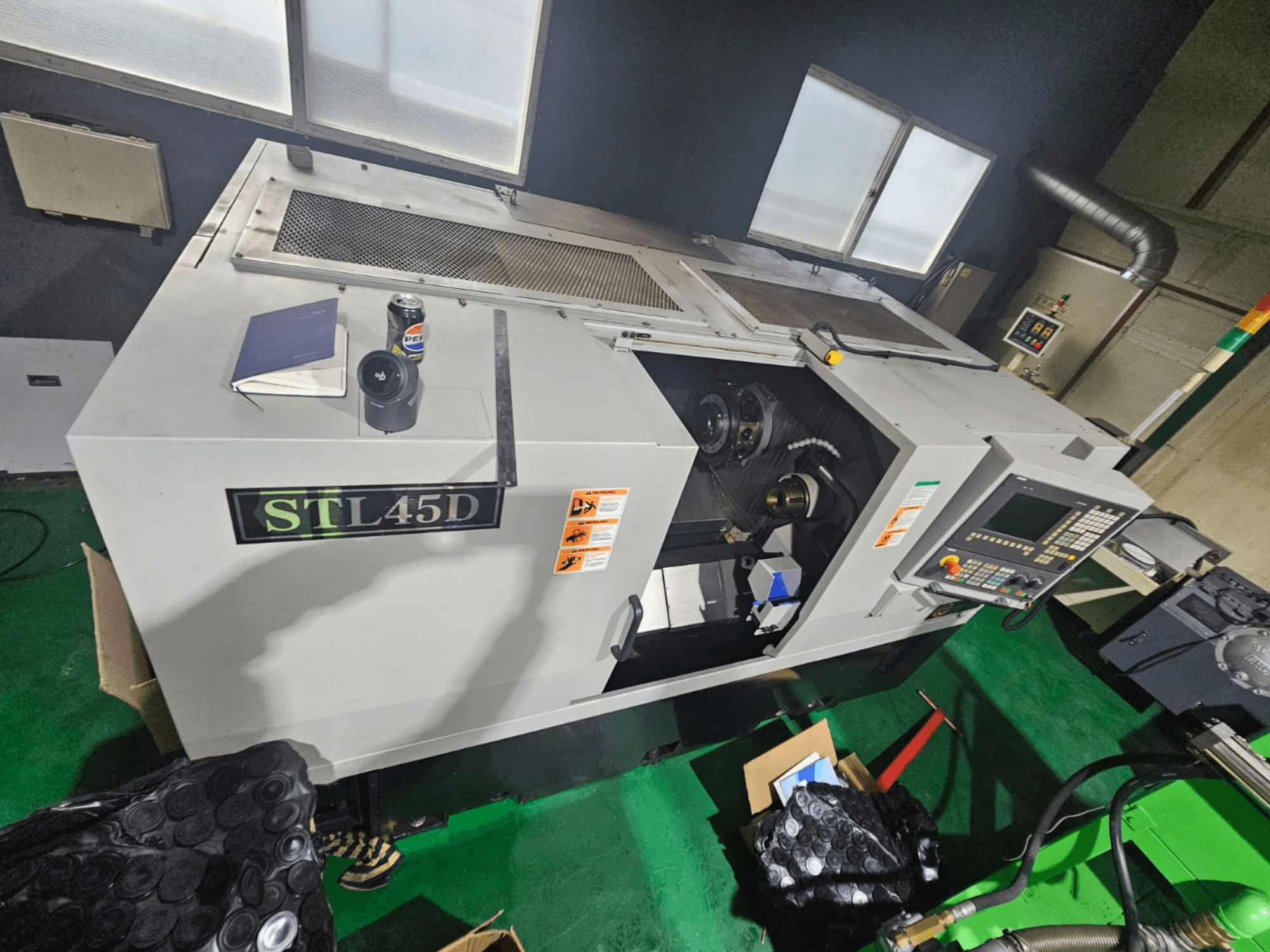 STL45D CNC darbagalds, skatīts no augšas, redzams vadības panelis, cilindriska detaļa, piezīmjdators un kanna virsū.