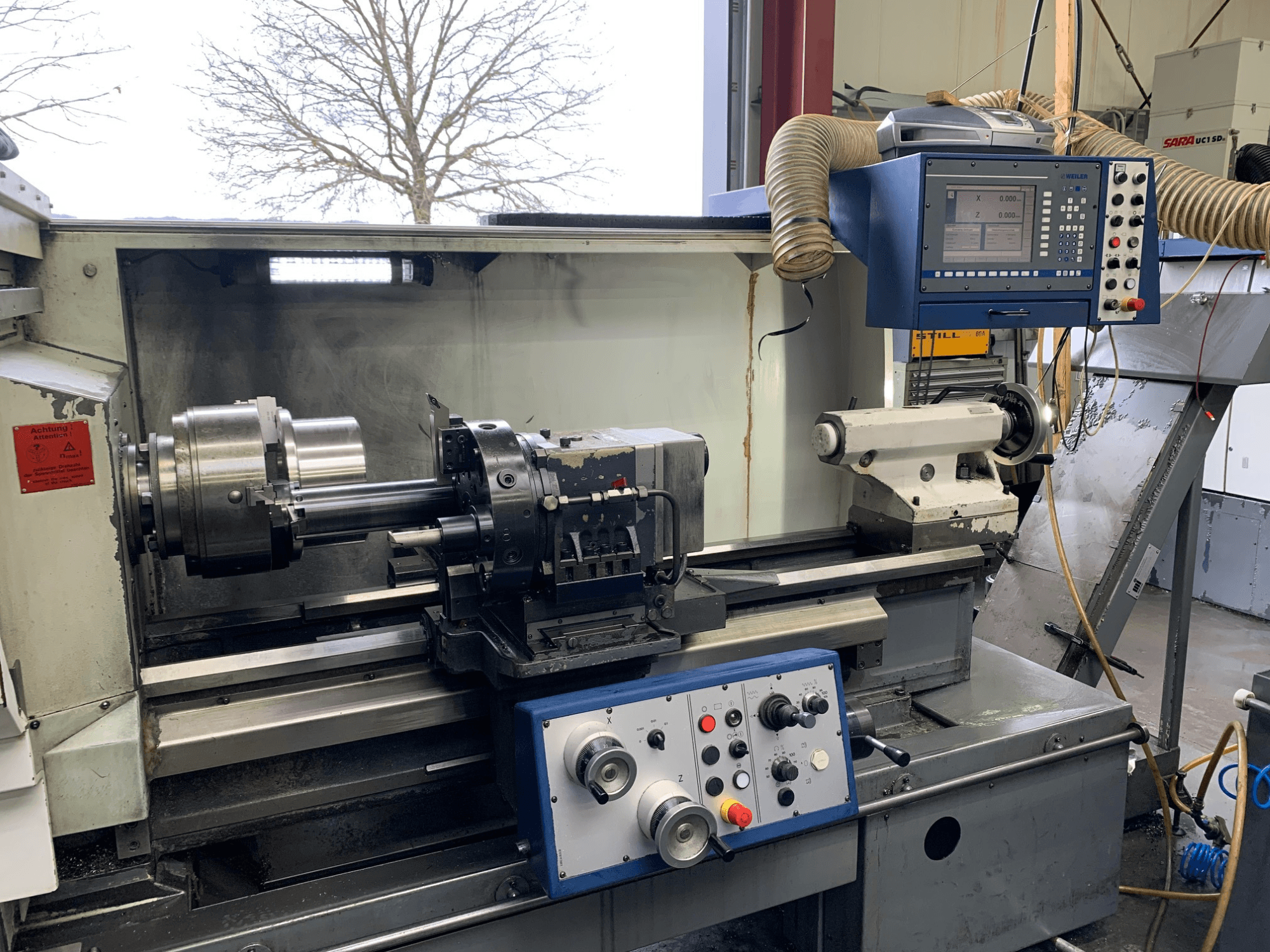 Weiler E55X1000 horizontālās virpošanas darbgalds darbnīcā, kurā redzams vadības panelis, virpa un instrumentu turētājs. Skats no priekšpuses.