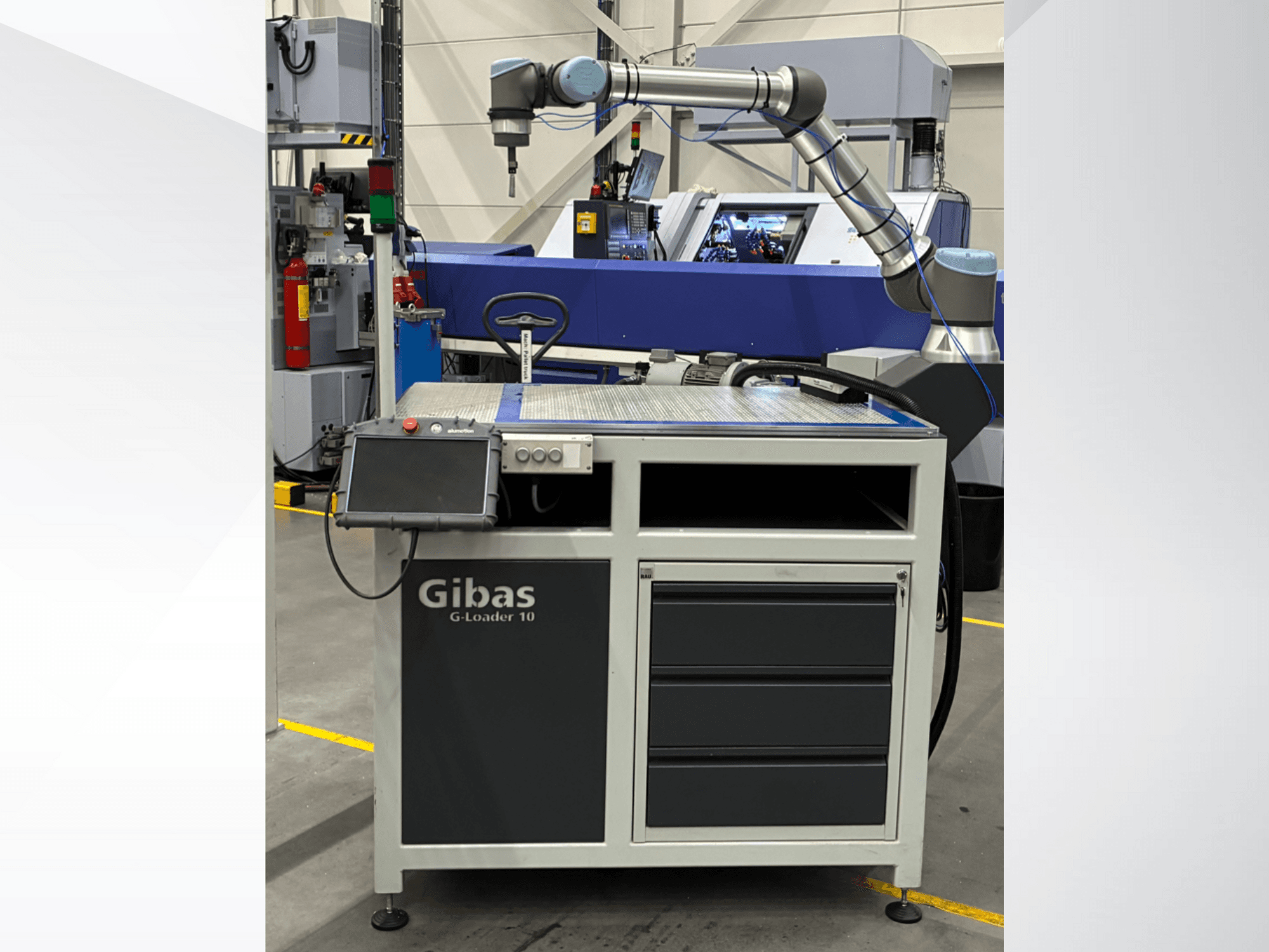 Gibas G-Loader 10 ar robotizēto roku, skats no priekšpuses; ar skārienjūtīgā ekrāna vadības funkciju un atvilktņu glabāšanu rūpnieciskā vidē.