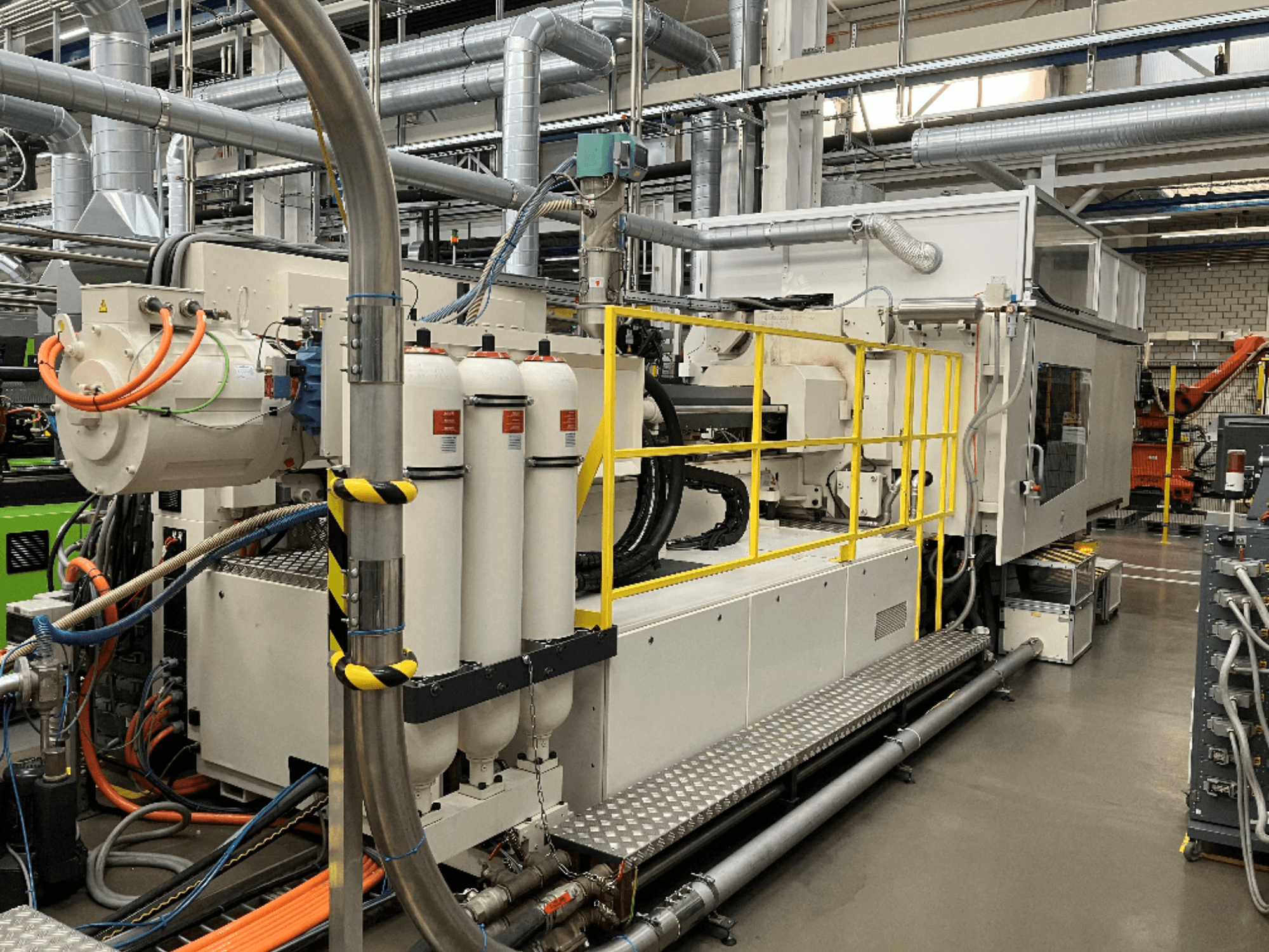 Rūpnieciskā mašīna ar baltu un pelēku korpusu, vairākām šļūtenēm un filtru tvertnēm; skats no sāniem, kas parāda darbības iestatījumus.