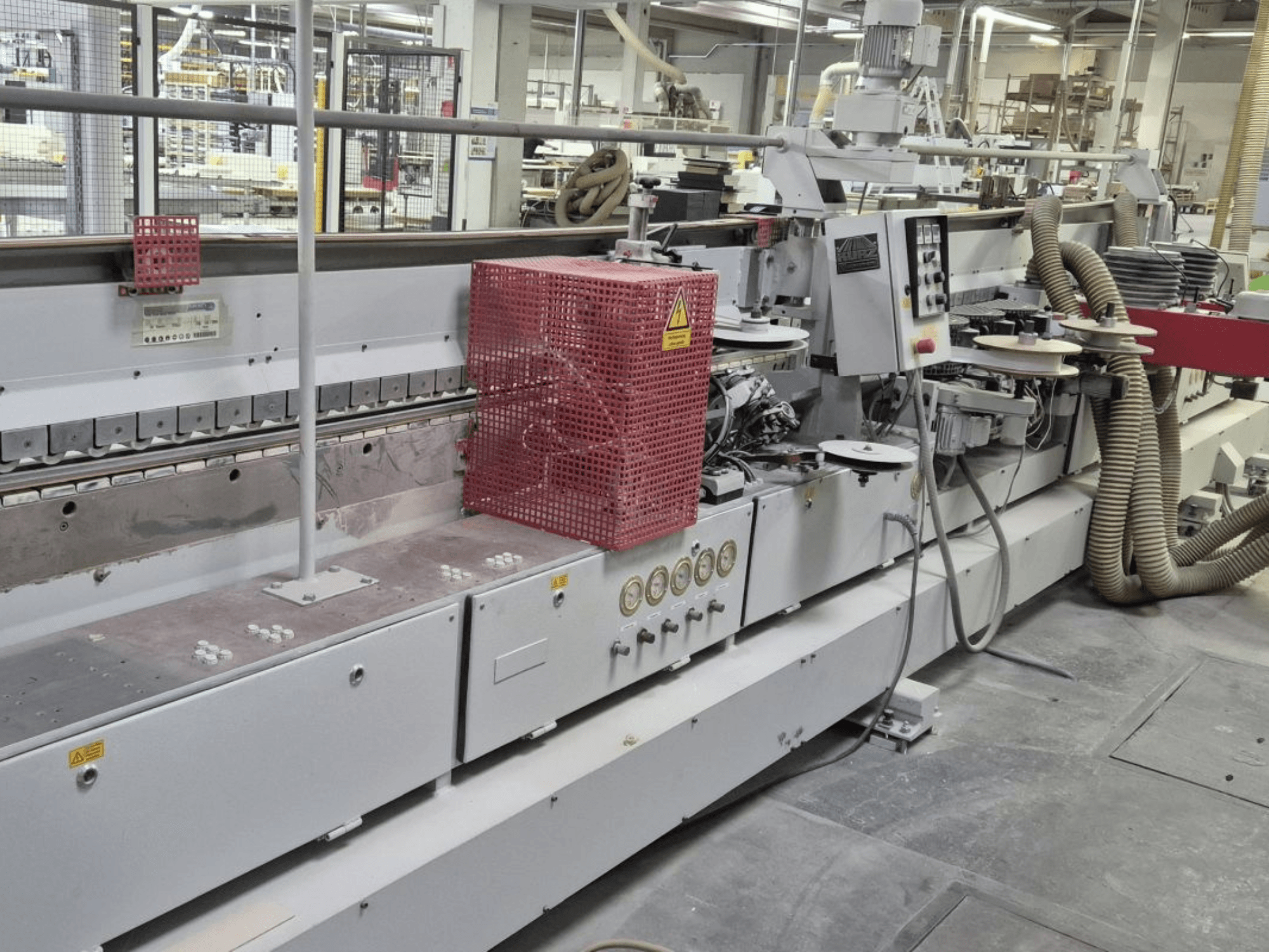 Malu aplīmēšanas iekārta ar vadības paneli, sūkšanas šļūtenēm un sarkanu drošības pārsegu, skatīts no sānu leņķa.