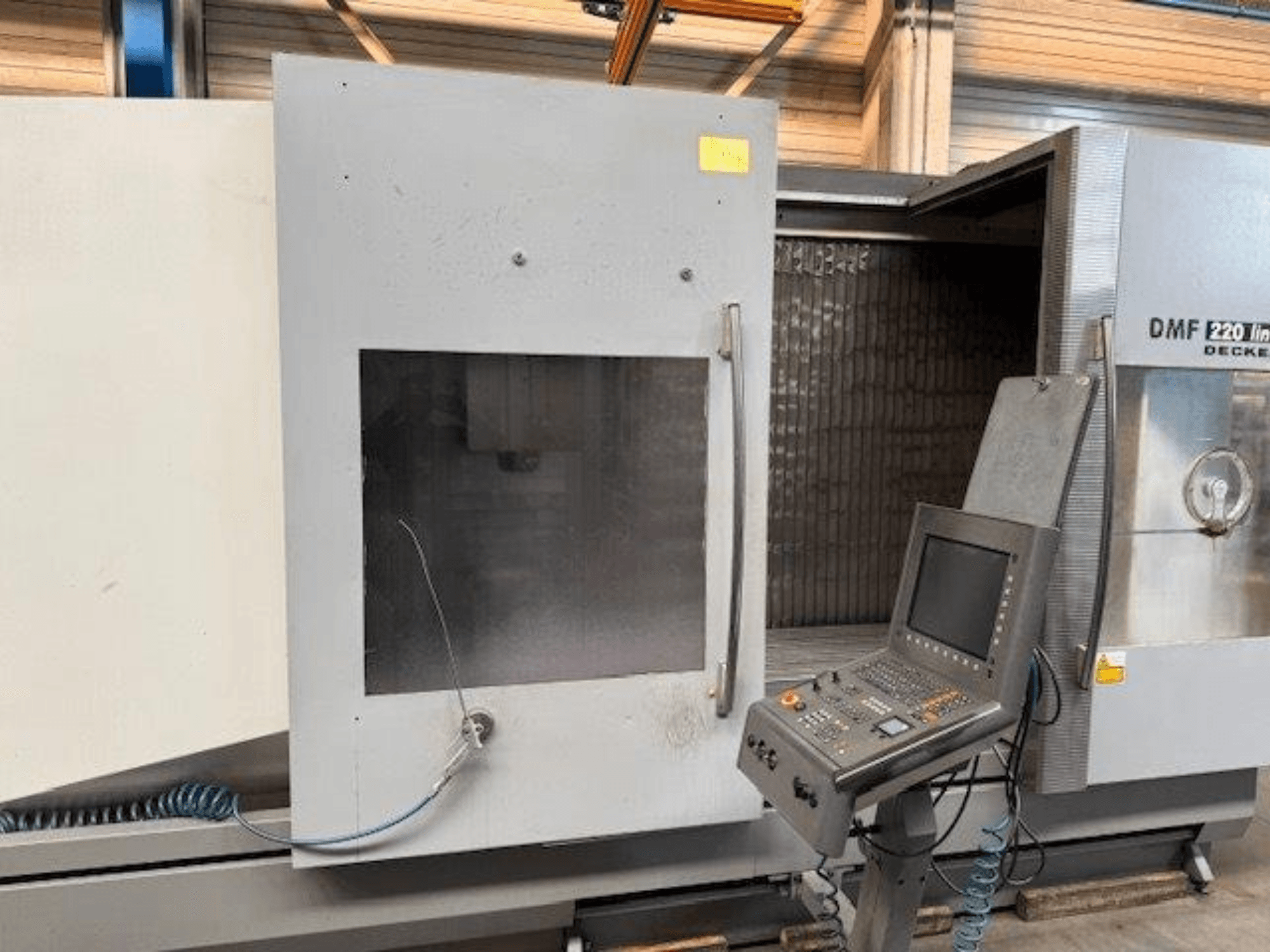 DECKEL MAHO DMF 220 lineārā vertikālā apstrādes centra priekšējais skats, kurā redzams vadības panelis un atvērtas mašīnas durvis.