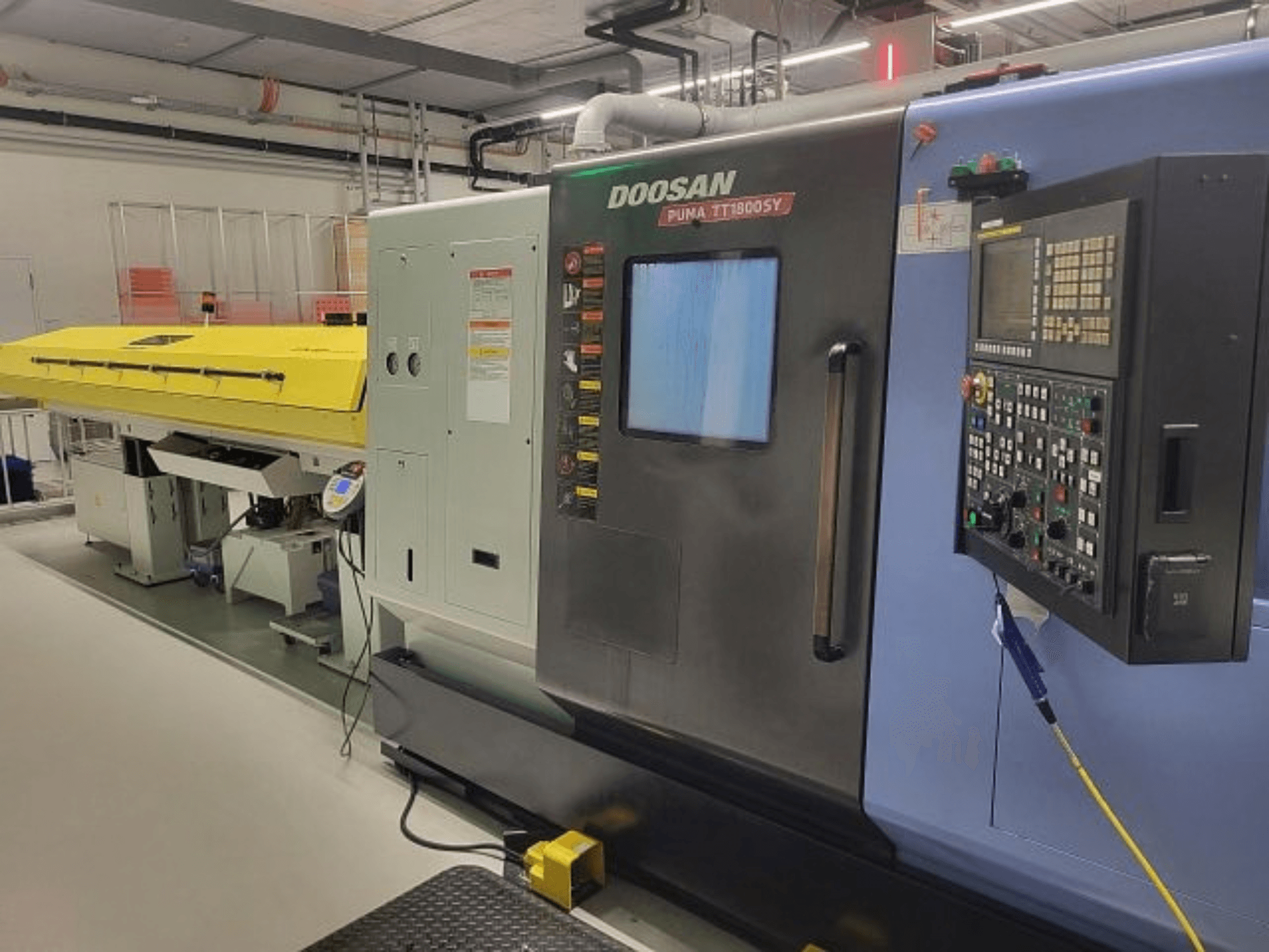 DOOSAN PUMA TT 1800 SY virpošanas un frēzēšanas centrs, skats no priekšpuses ar vadības pulti un dzeltenu pārsegu, rūpnieciskā vidē.