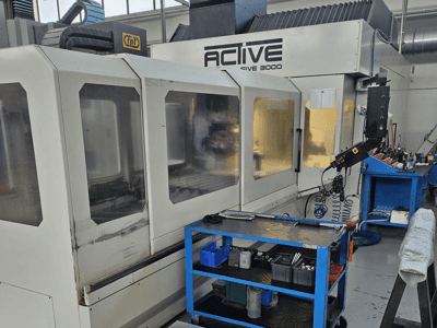 Active 3000 CNC darbnīcā, skats no priekšpuses ar instrumentiem uz zila ratiņa, redzamas vadības ierīces un darba zona darbnīcā.