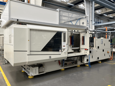 Sānu skats uz AET modeļa iesmidzināšanas formēšanas iekārtu ar vadības paneli un caurspīdīgiem vākiem rūpnieciskā vidē.