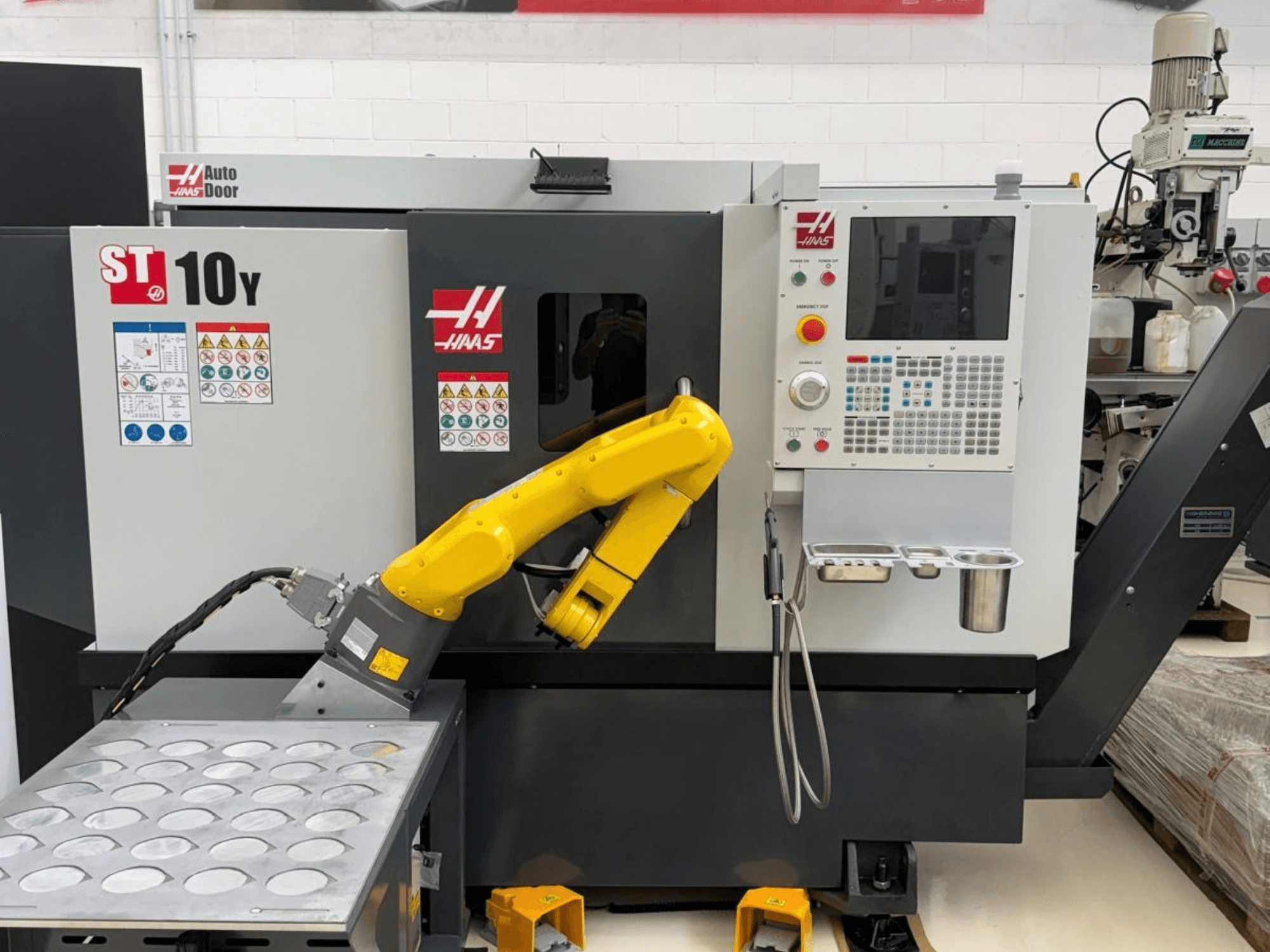 Haas ST-10Y horizontālā virpošanas mašīna, skatīta no priekšpuses, ar robotizētu manipulatoru un vadības paneli ar instrumentu turētāju plauktiem.