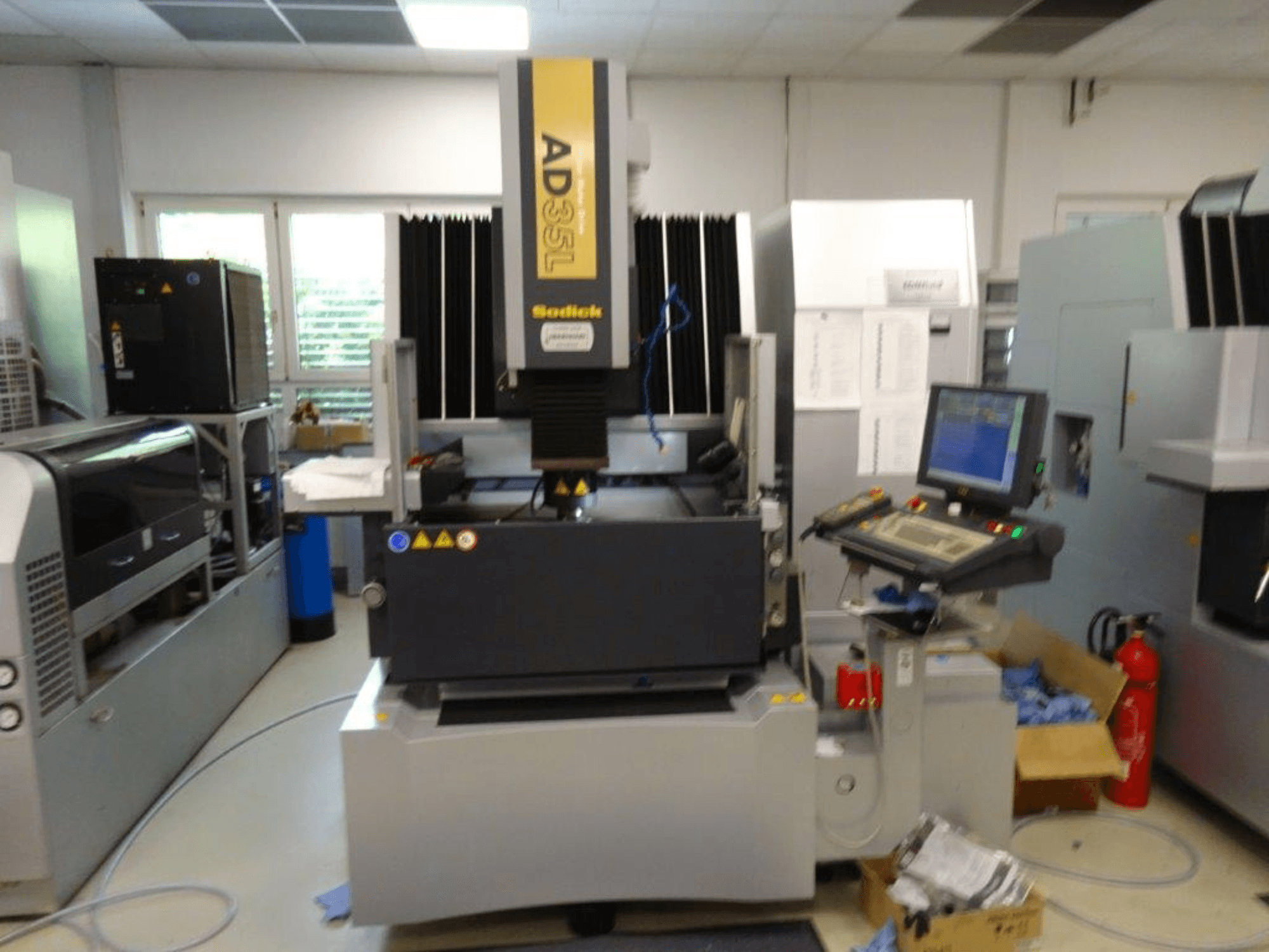 Sodick AD35L CNC mašīna no priekšpuses, ar vadības paneli, dzesēšanas bloku un drošības indikatoriem.