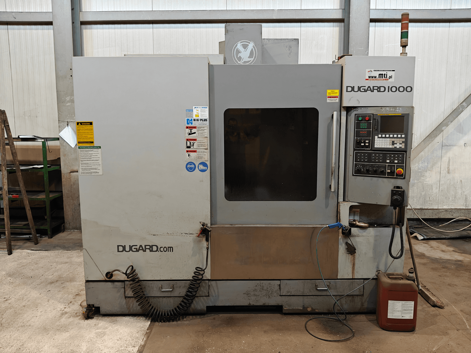 Dugard 1000 CNC mašīna, priekšējais skats, kurā redzams vadības panelis, drošības marķējums un eļļas tvertne, darbnīcā.