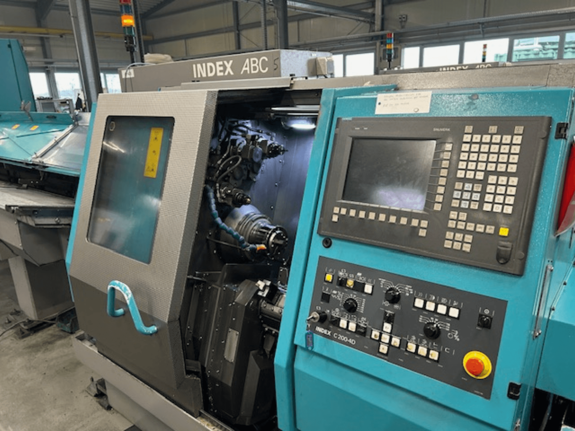 INDEX C200-AD CNC virpas priekšējais skats ar vadības paneli, redzamajām iekšējām sastāvdaļām un drošības elementiem.