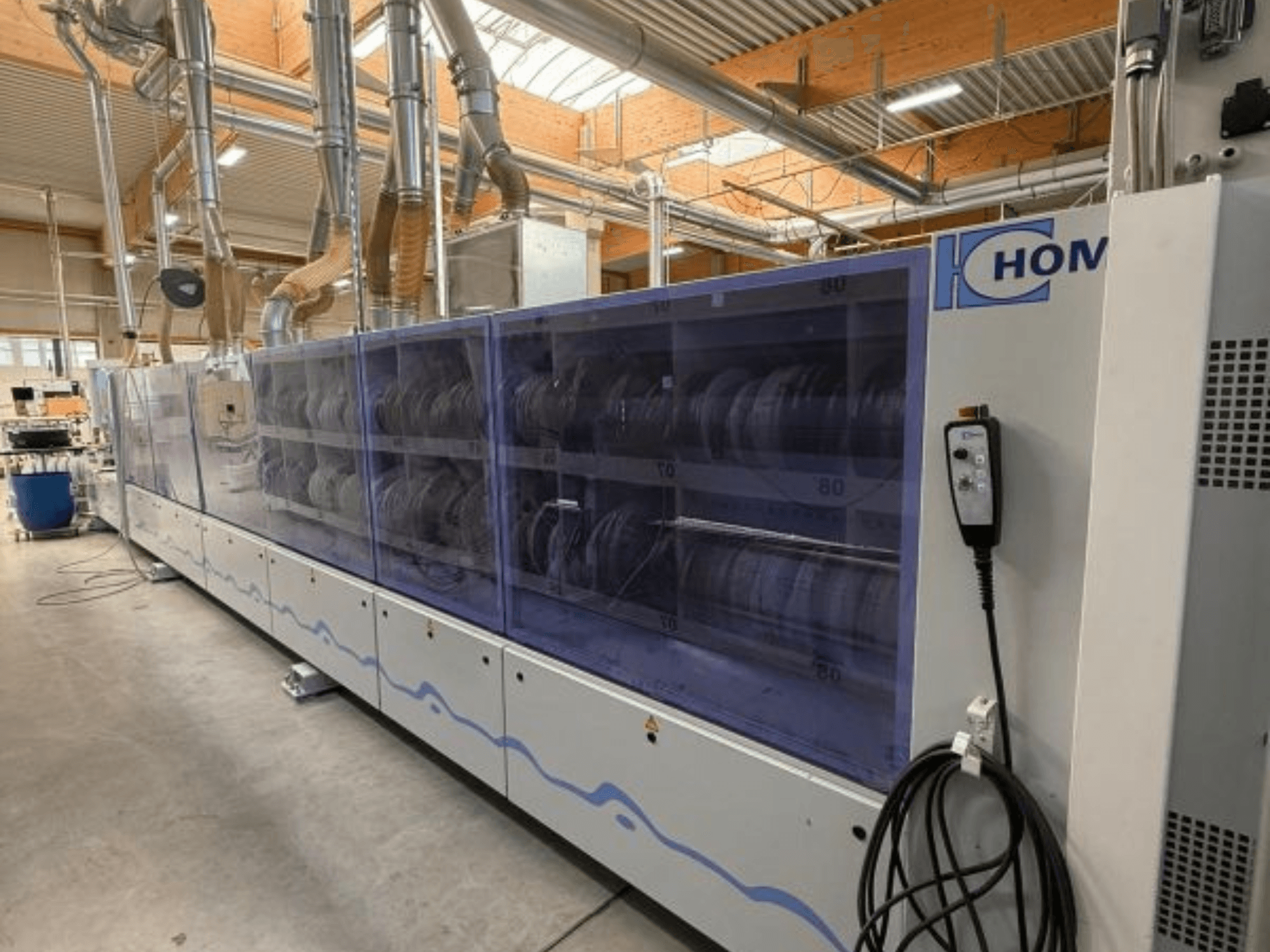 Rūpnieciskā veļas mazgājamā mašīna HOM, skats no priekšpuses, ar caurspīdīgu paneli, uz kura redzami trauki; vadības panelis ar pogām sānos.