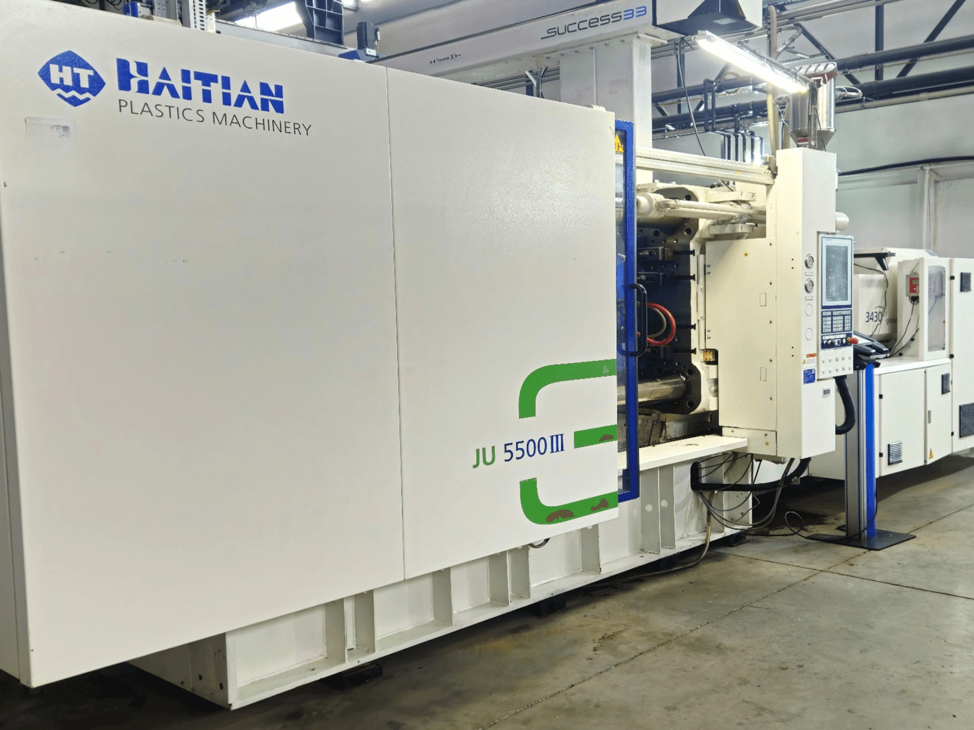 Haitian JU 5500III plastmasas apstrādes iekārta rūpnīcā, priekšējais skats, kurā redzams vadības panelis un ražošanas zona.