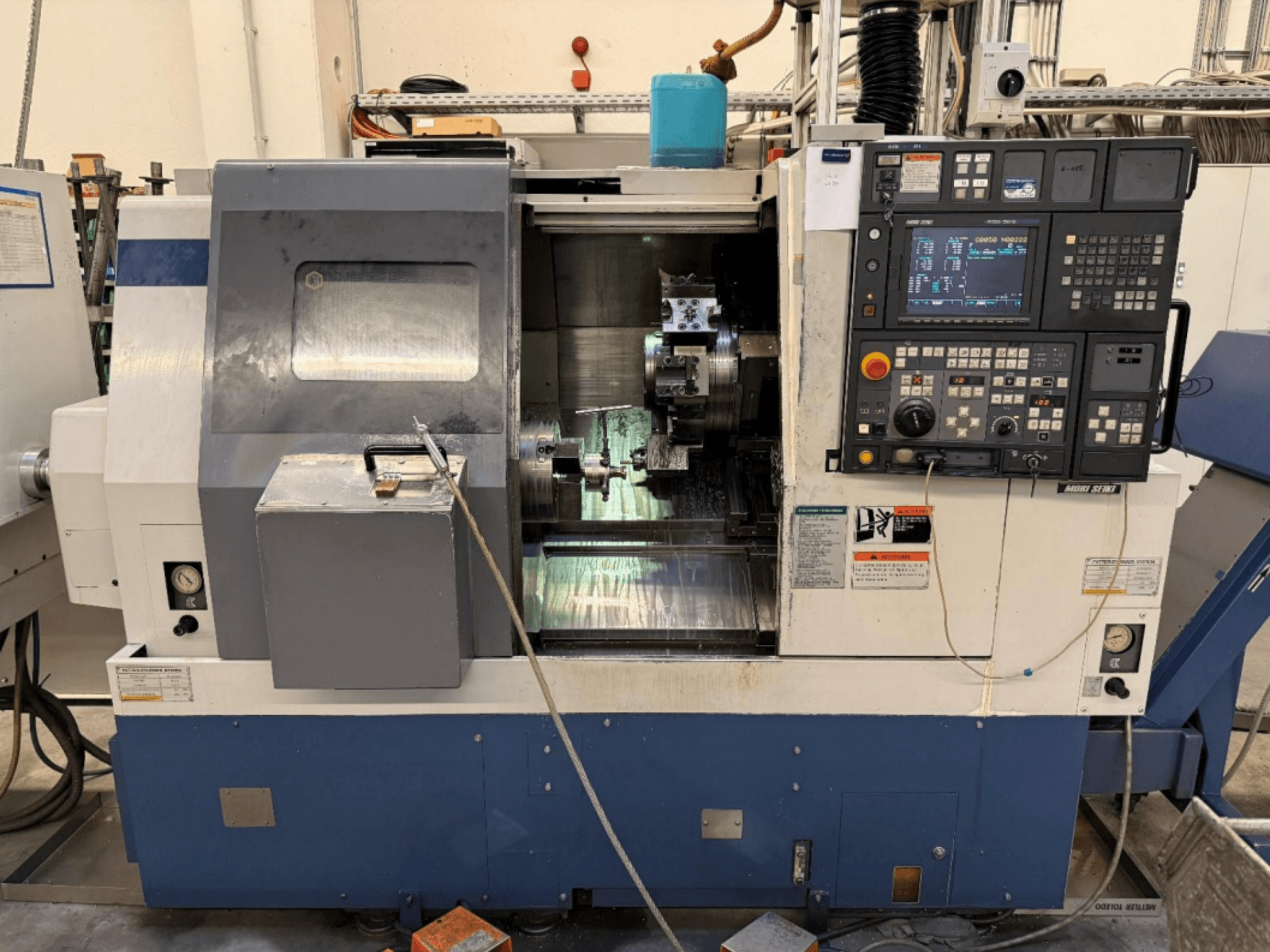 MORI SEIKI SL-250ASMC virpošanas un frēzēšanas centrs, skats no priekšpuses, kurā redzams vadības panelis un darba gabala skava darbības laikā.