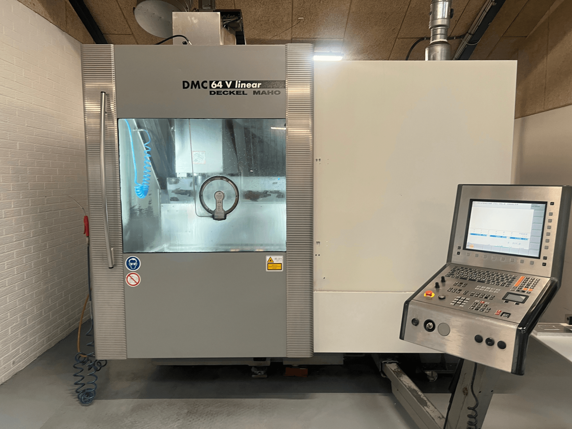 Deckel Maho DMC 64 V Linear, CNC apstrādes centra priekšējais skats ar redzamu vadības paneli un dzesēšanas šķidruma sprauslu.