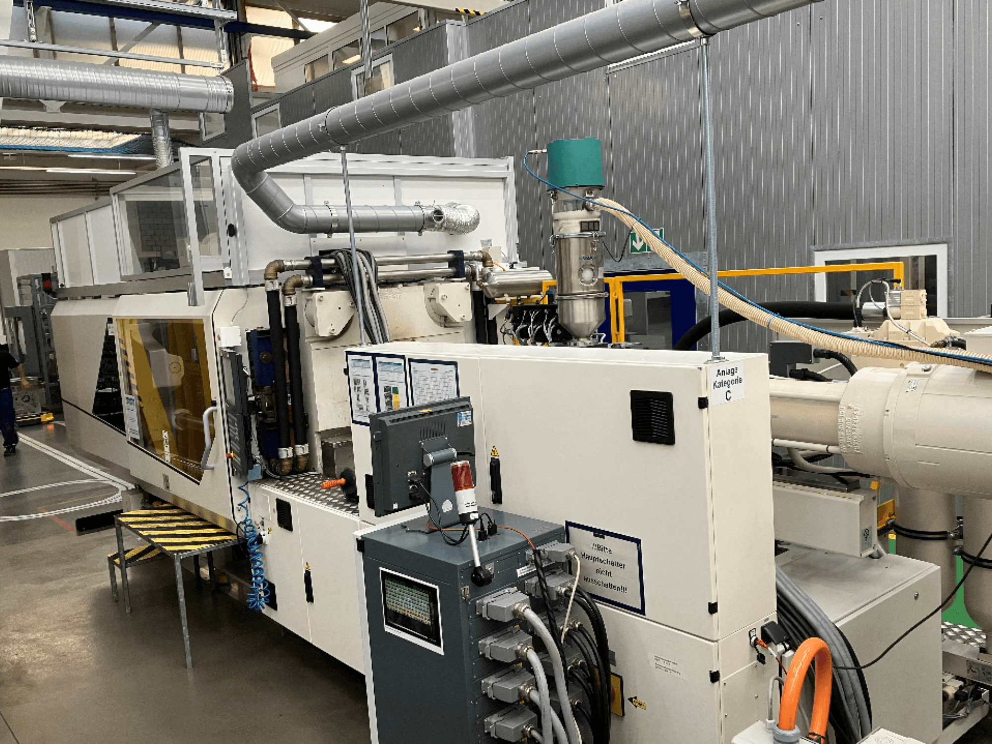 Iesmidzināšanas veidošanas iekārta, skats no priekšpuses, ar zīmola marķējumu, vadības paneli un redzamām šļūtenēm rūpnīcā.