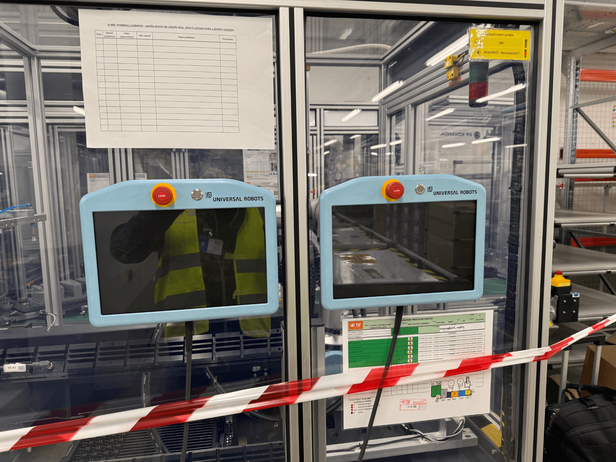 Universal Robots UR5 e robota rokas vadības panelis ar diviem monitoriem, avārijas apturēšanas pogām un drošības instrukcijām.