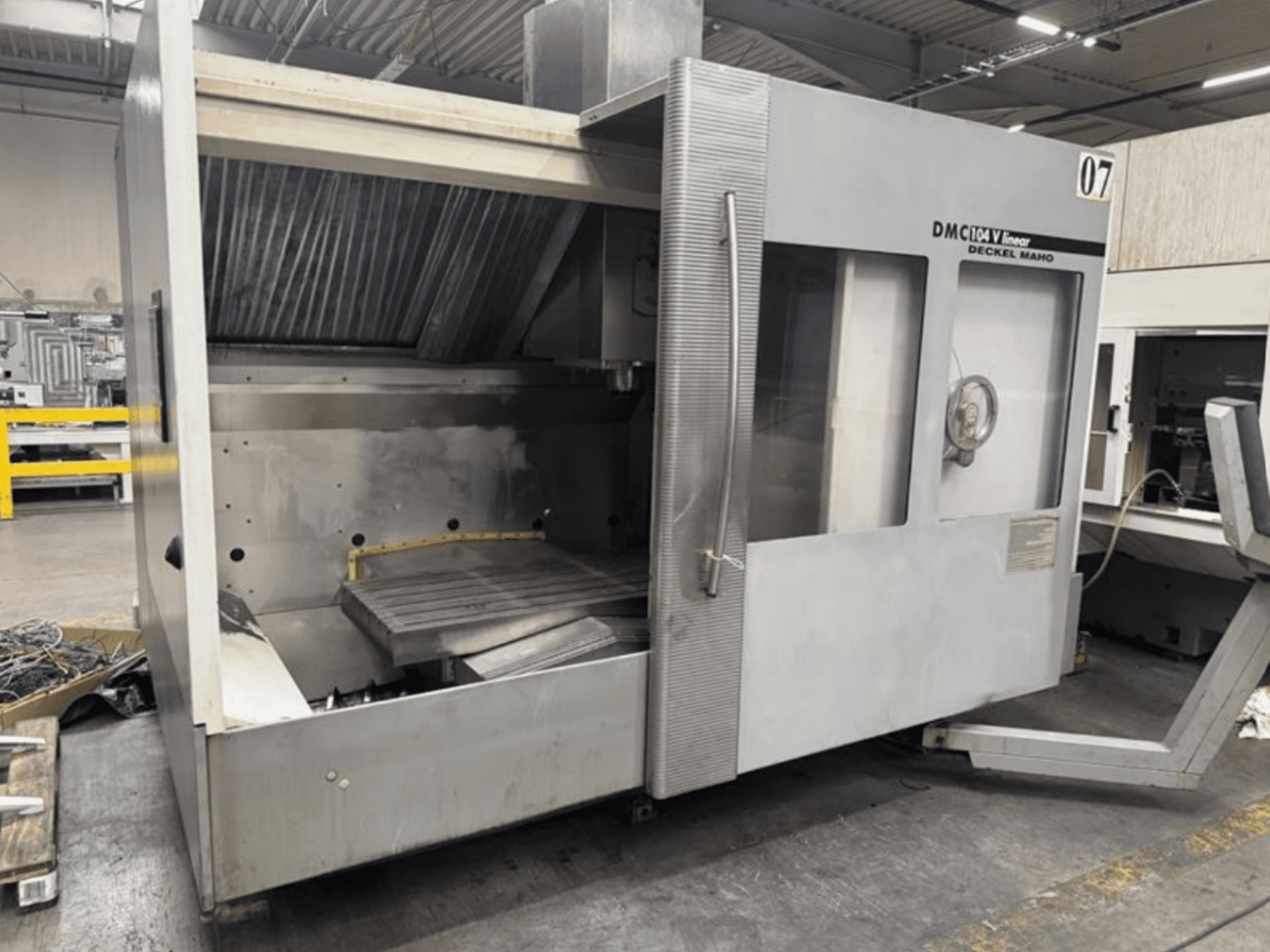 Deckel Maho DMC 104 V lineārā mašīna, skats no priekšpuses, ar tukšu apstrādes zonu un lielu darba galdu.