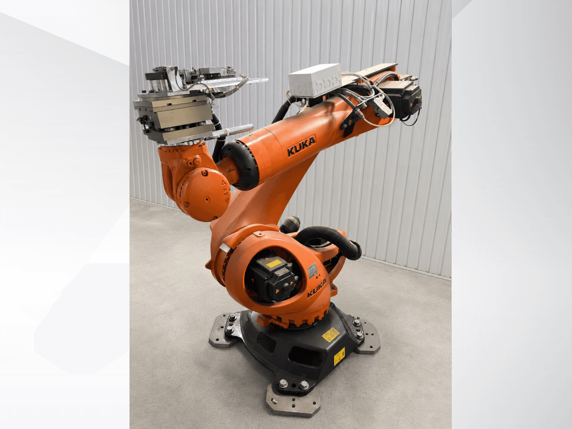 Papildu KUKA KR 90 R3100 robota roka oranžā krāsā, skats no sāniem, kurā redzami savienojumi, vadības bloks un instrumenta stiprinājums uz gala efektora.