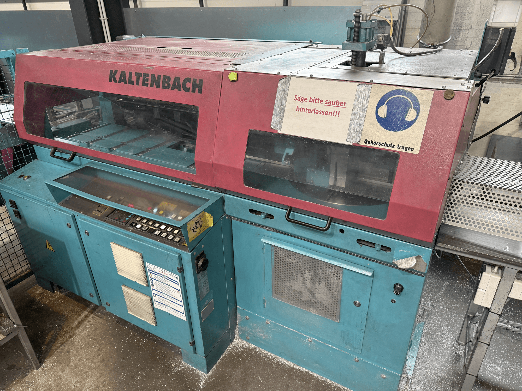 KALTENBACH rūpnieciskā griešanas iekārta, skats no priekšpuses, ar vadības paneli un drošības zīmi dzirdes aizsardzībai.