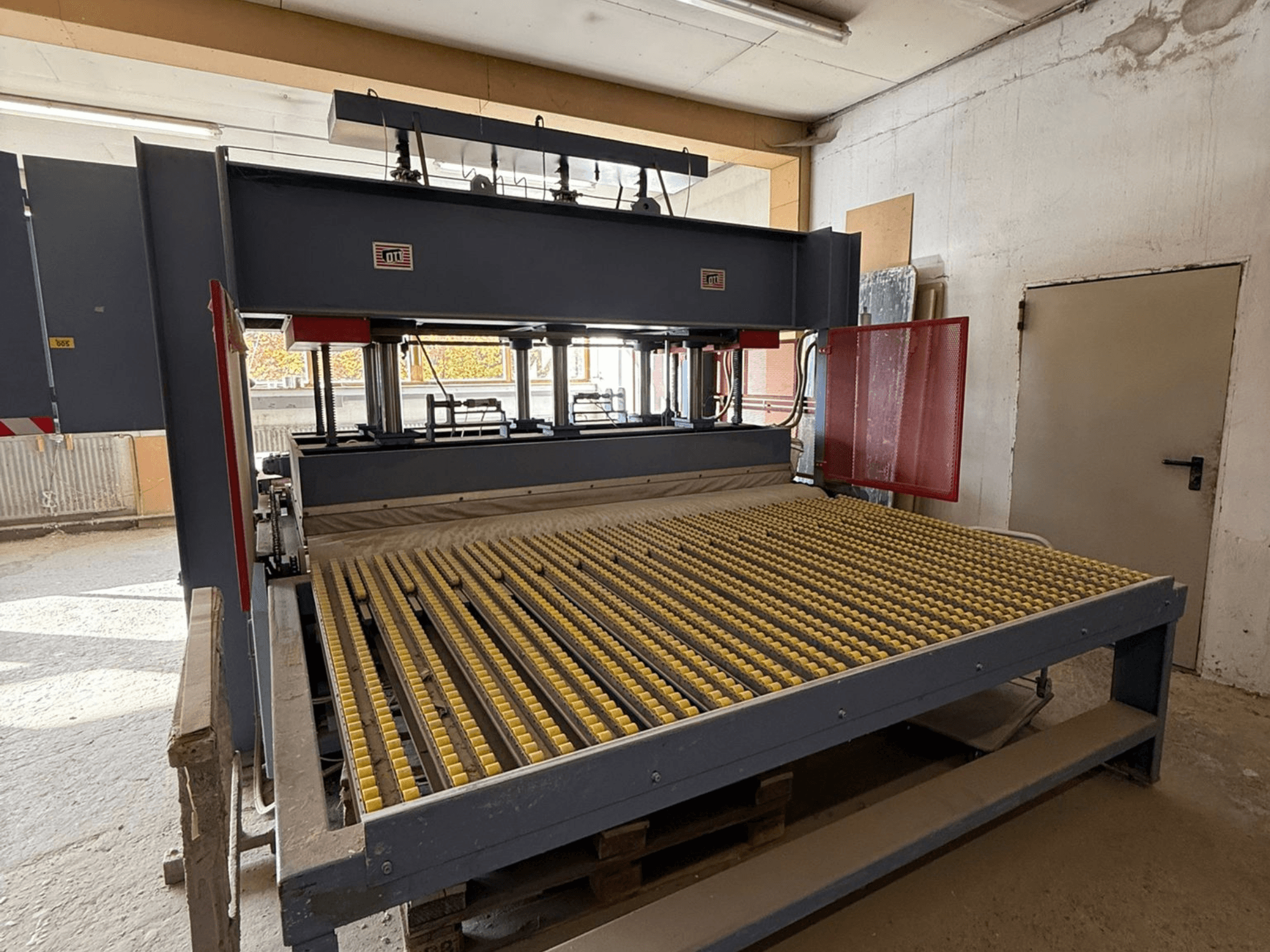 Rūpnieciskā mašīna ar dzelteniem veltņiem, skats no priekšpuses, redzams zīmola logotips, ko izmanto materiālu apstrādei darbnīcā.