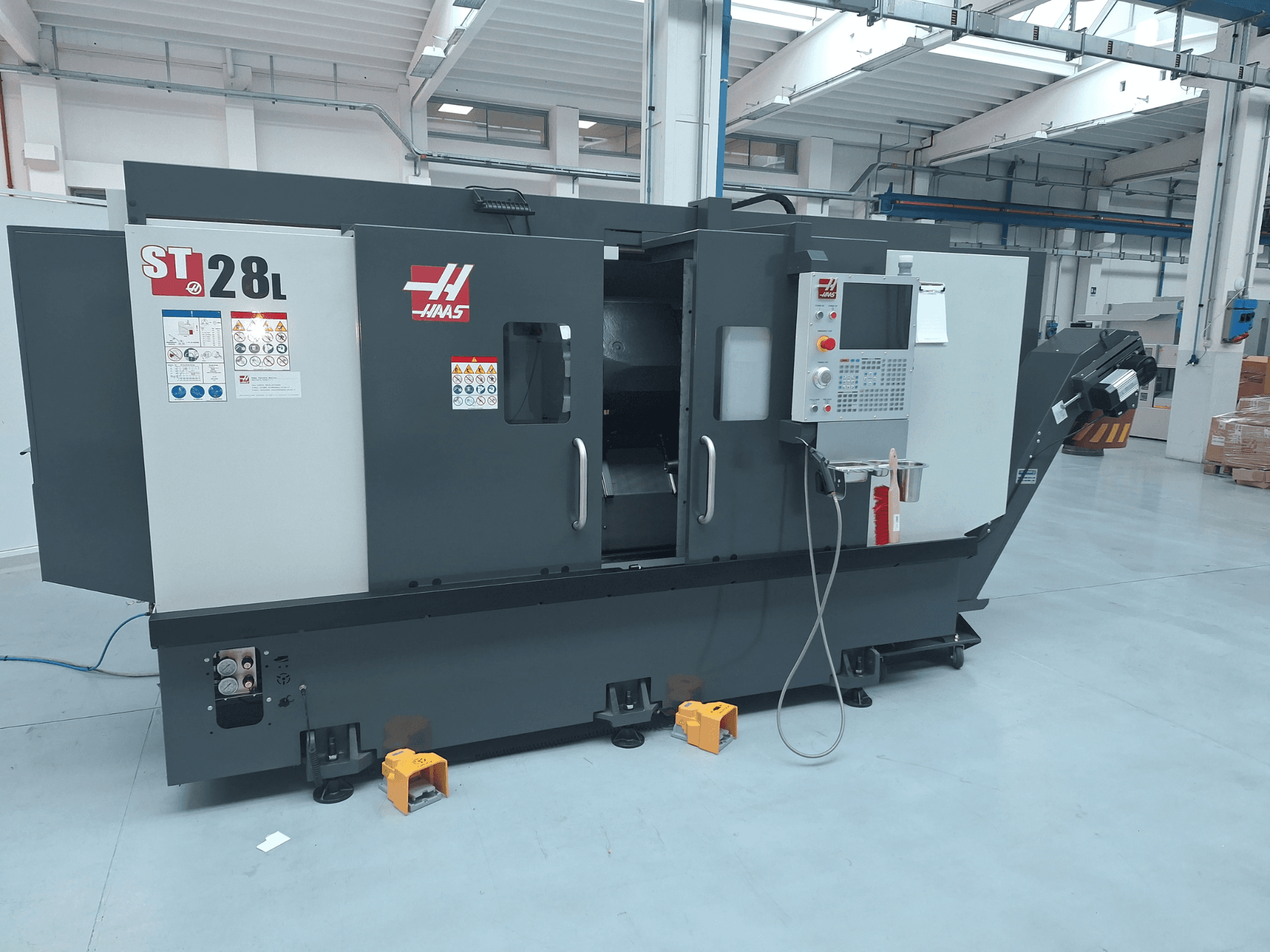 Haas ST-28L horizontālās virpošanas mašīnas sānskats, kurā redzams vadības panelis, darbības pogas un drošības uzlīmes.