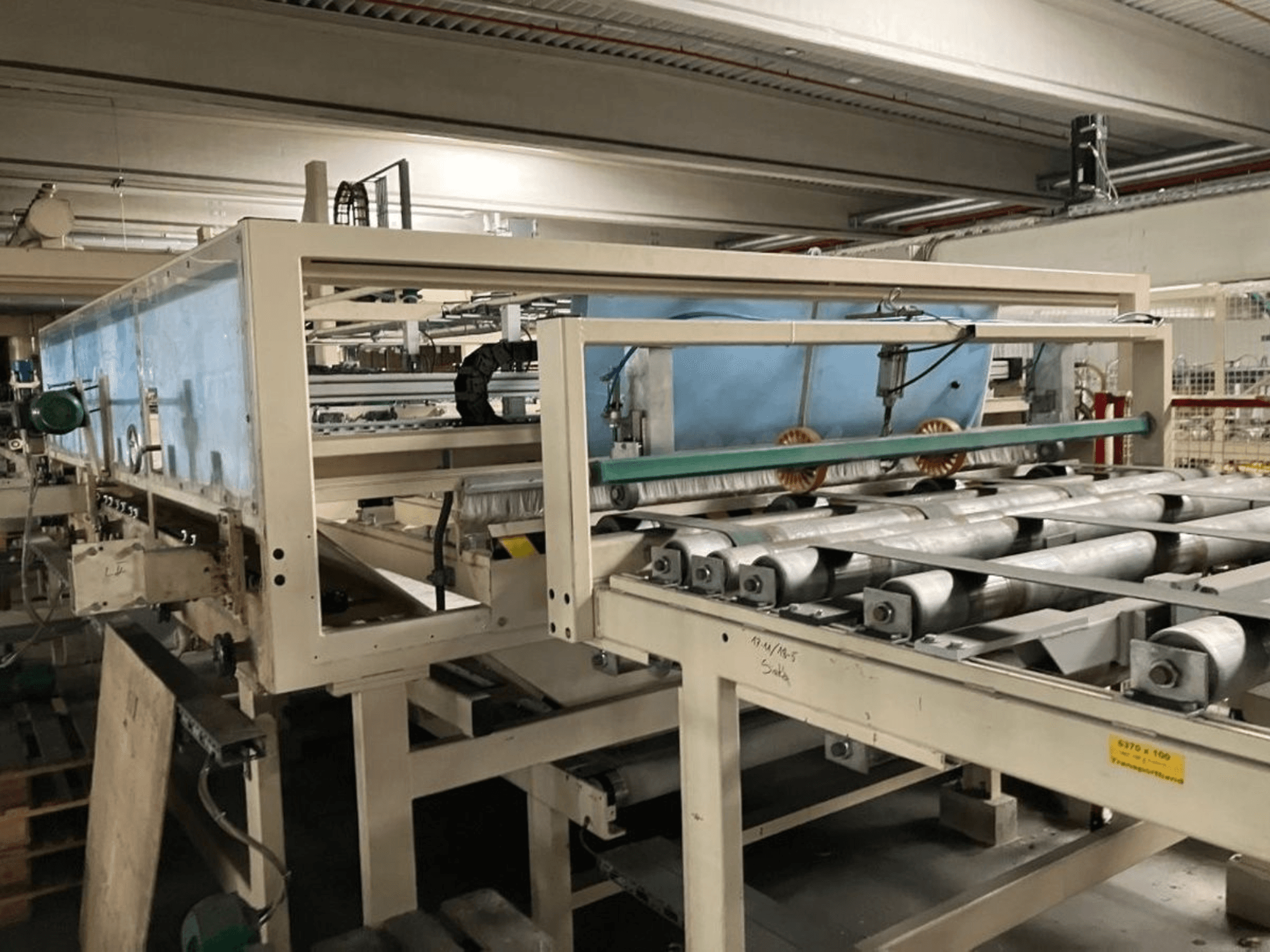 WEMHÖNER KT-F-1E laminēšanas prese, skats no sāniem, ar veltņiem un vadības ierīcēm materiālu apstrādei rūpnīcā.