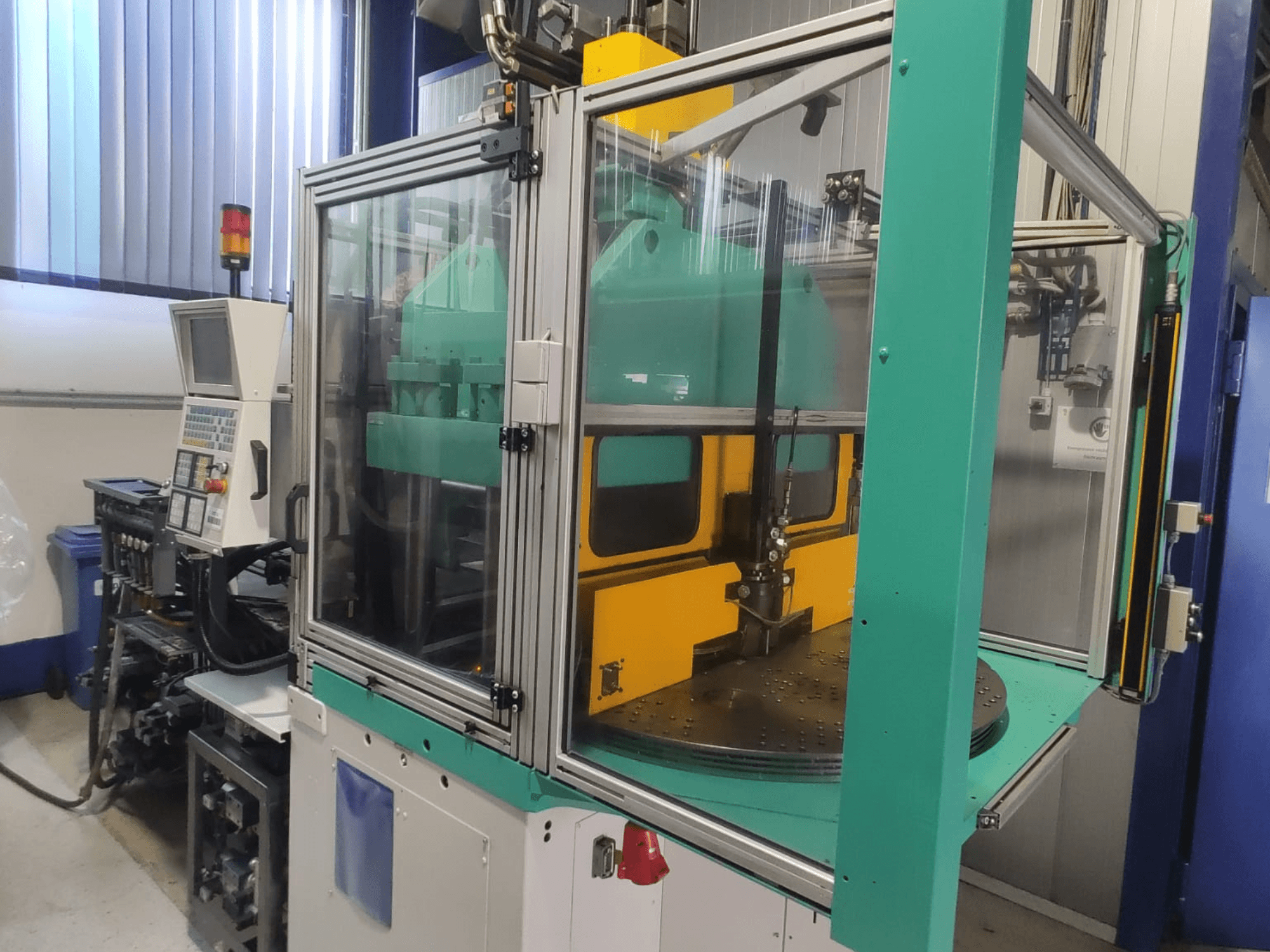 Vertikālā plastmasas liešanas mašīna „Arburg 1200 TS 800-60-350“, skats no priekšpuses, kurā redzams vadības panelis un drošības apvalks.
