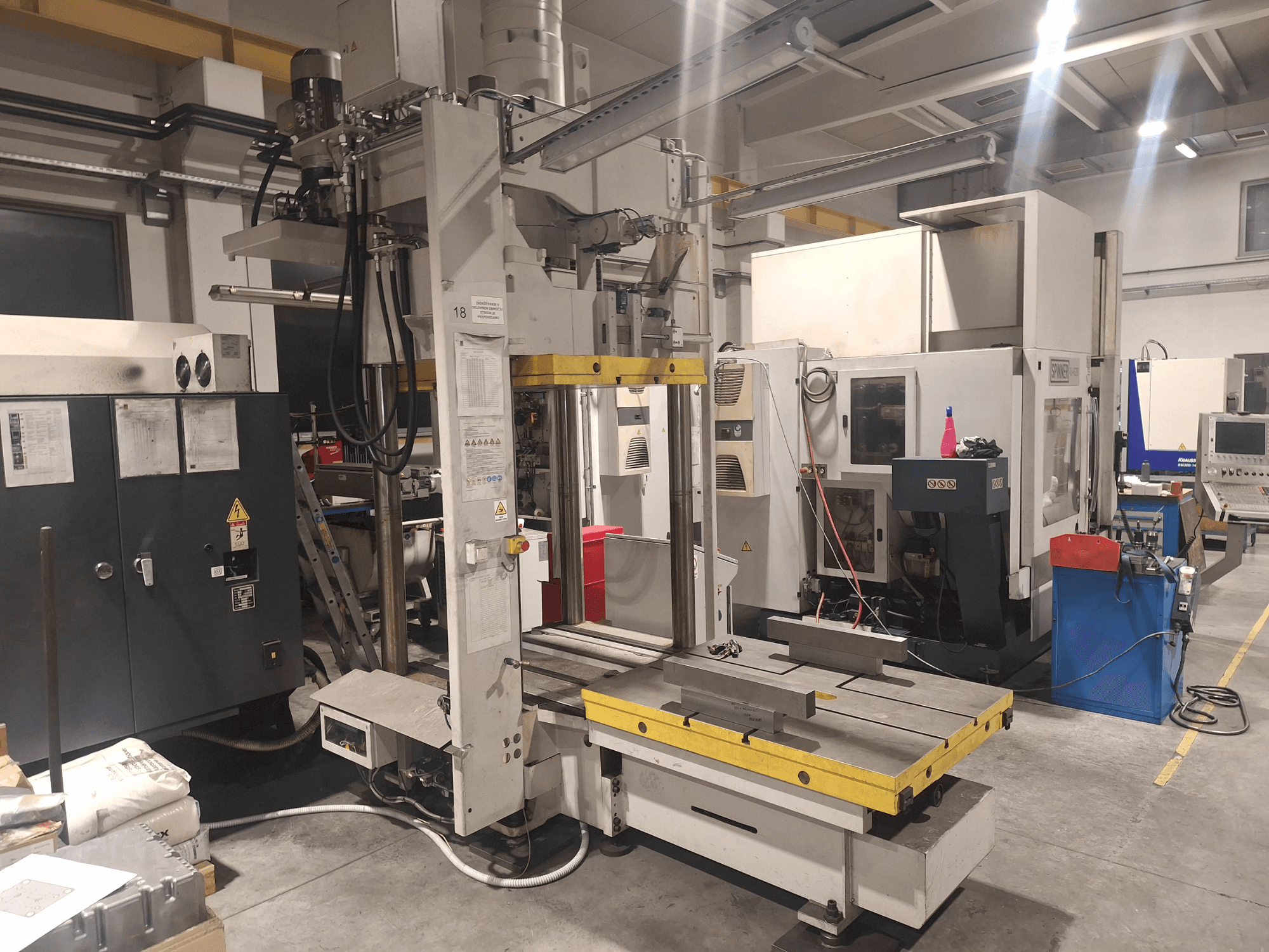 Horizontālā frēzmašīna Synergic, skats no priekšpuses; ar plašu galdu un dažādiem vadības paneļiem darbnīcā.