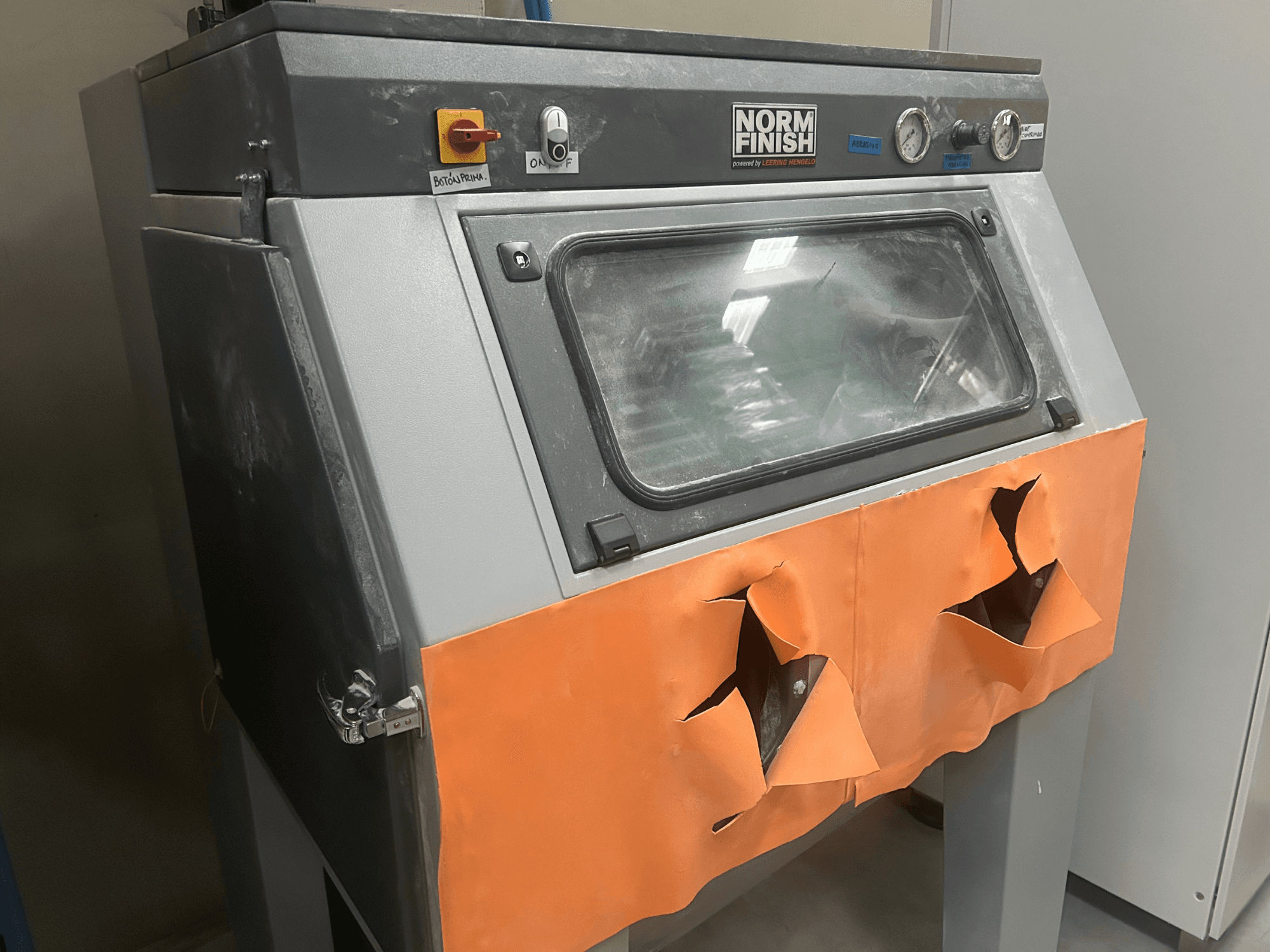 EOS P 396 plastmasas 3D printeris pelēkā krāsā, skats no sāniem ar nolietotu oranžu vāku un redzamu vadības paneli, putekļains.