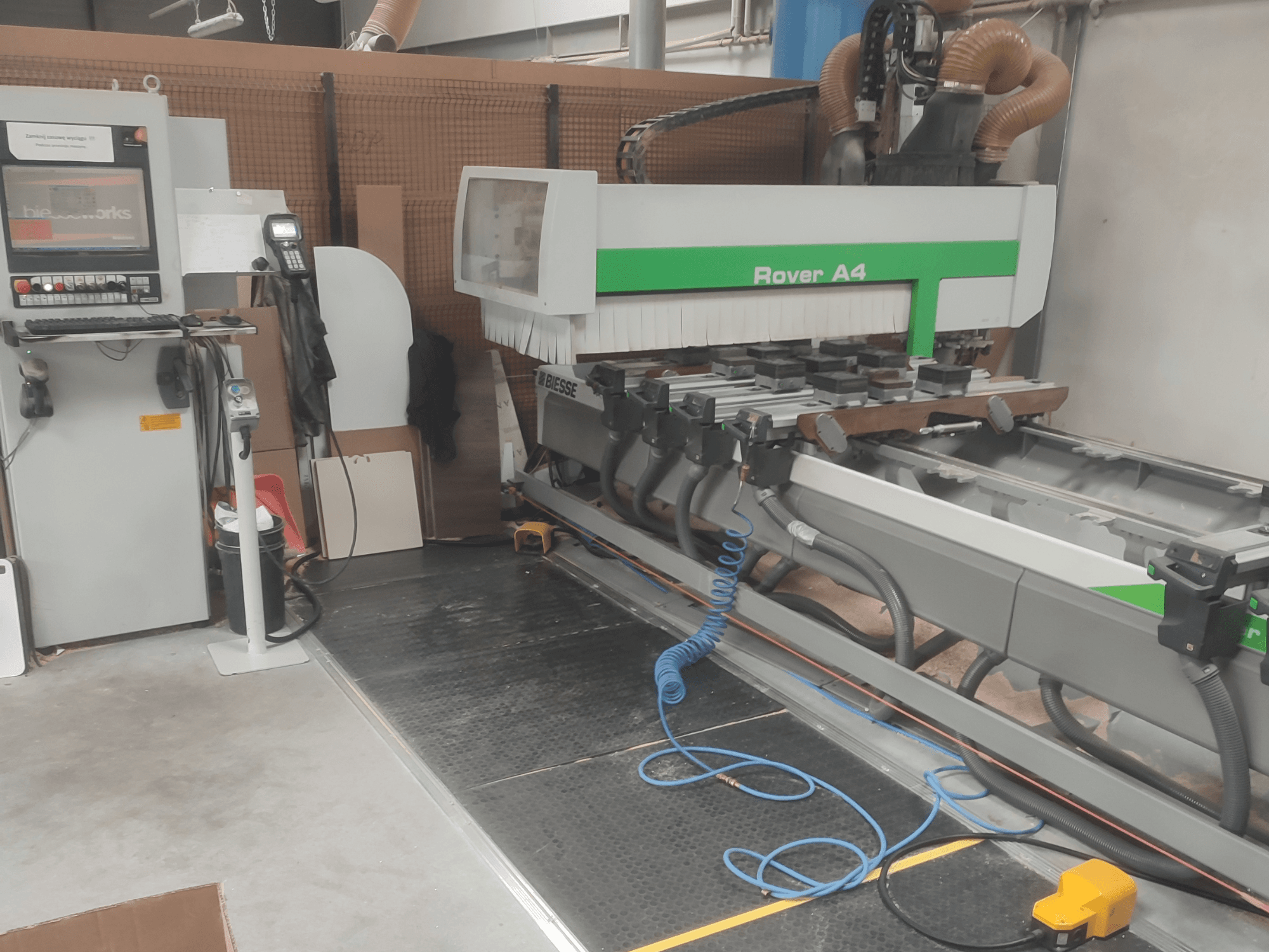 BIESSE Rover A4 CNC koka apstrādes centrs no sāniem, kurā redzams vadības panelis, vakuuma stiprinājumi un putekļu nosūces sistēma.