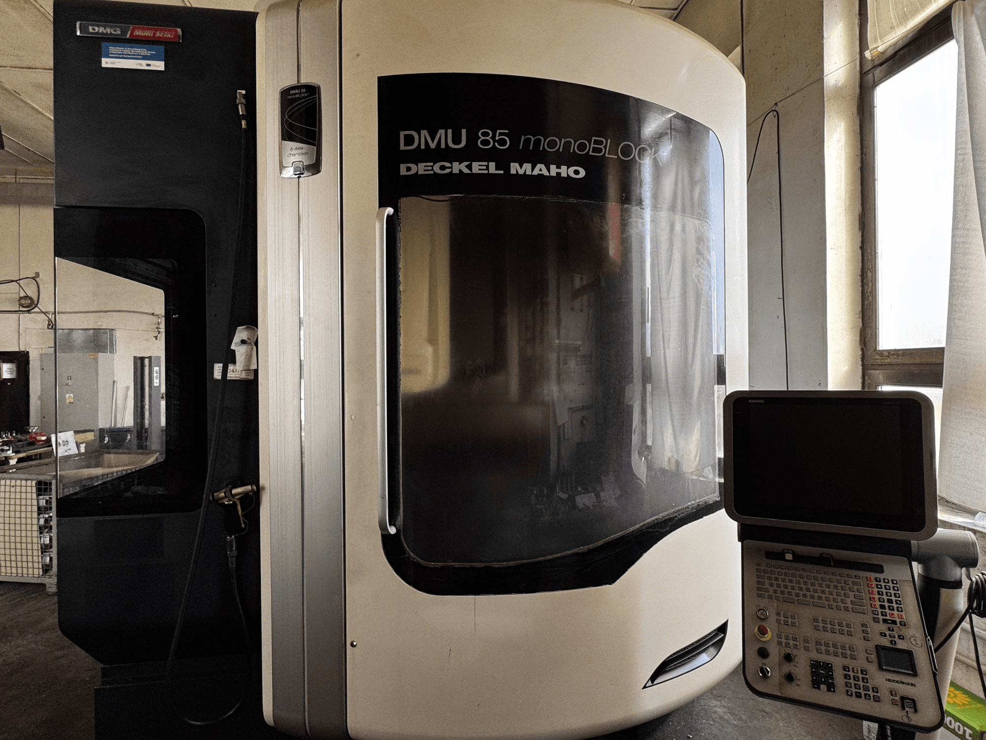 DMG MORI DMU 85 monoBLOCK vertikālais apstrādes centrs, skats no priekšpuses ar vadības paneli un lielu skatu logu.