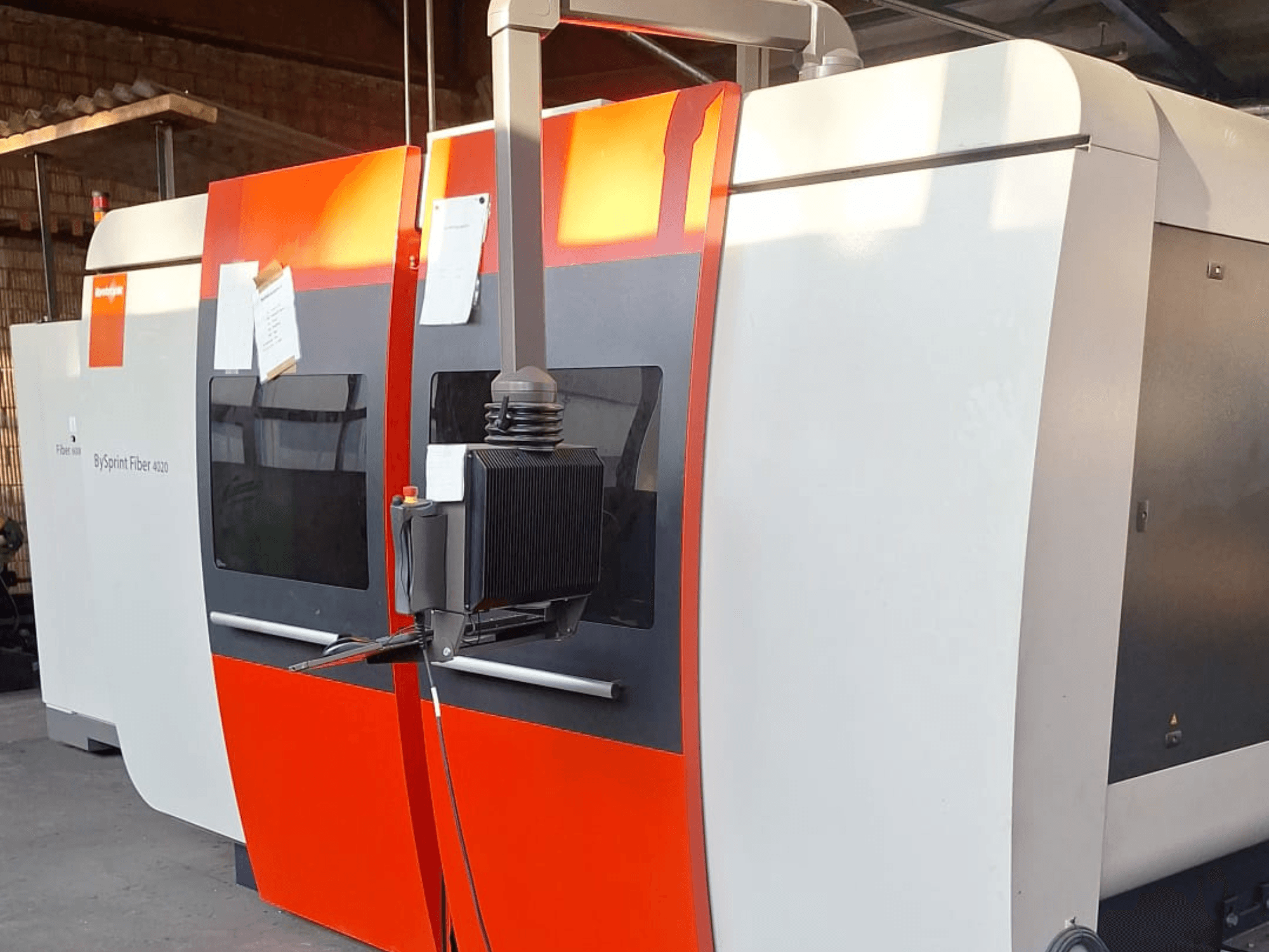 BySprint Fiber 4020 lāzera griešanas iekārta, skats no sāniem, ar sarkanbaltsarkanu ārpusi, redzams detalizēts vadības panelis.
