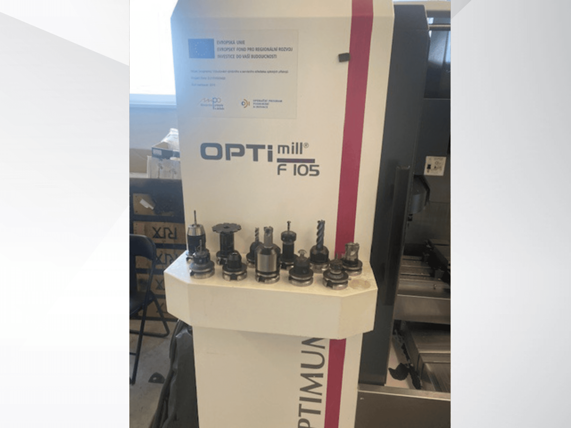 Vertikālā apstrādes centra „Optimum Optimill F105“ skats no priekšpuses, ar dažādiem pievienotiem instrumentiem, kas redzami sānos.