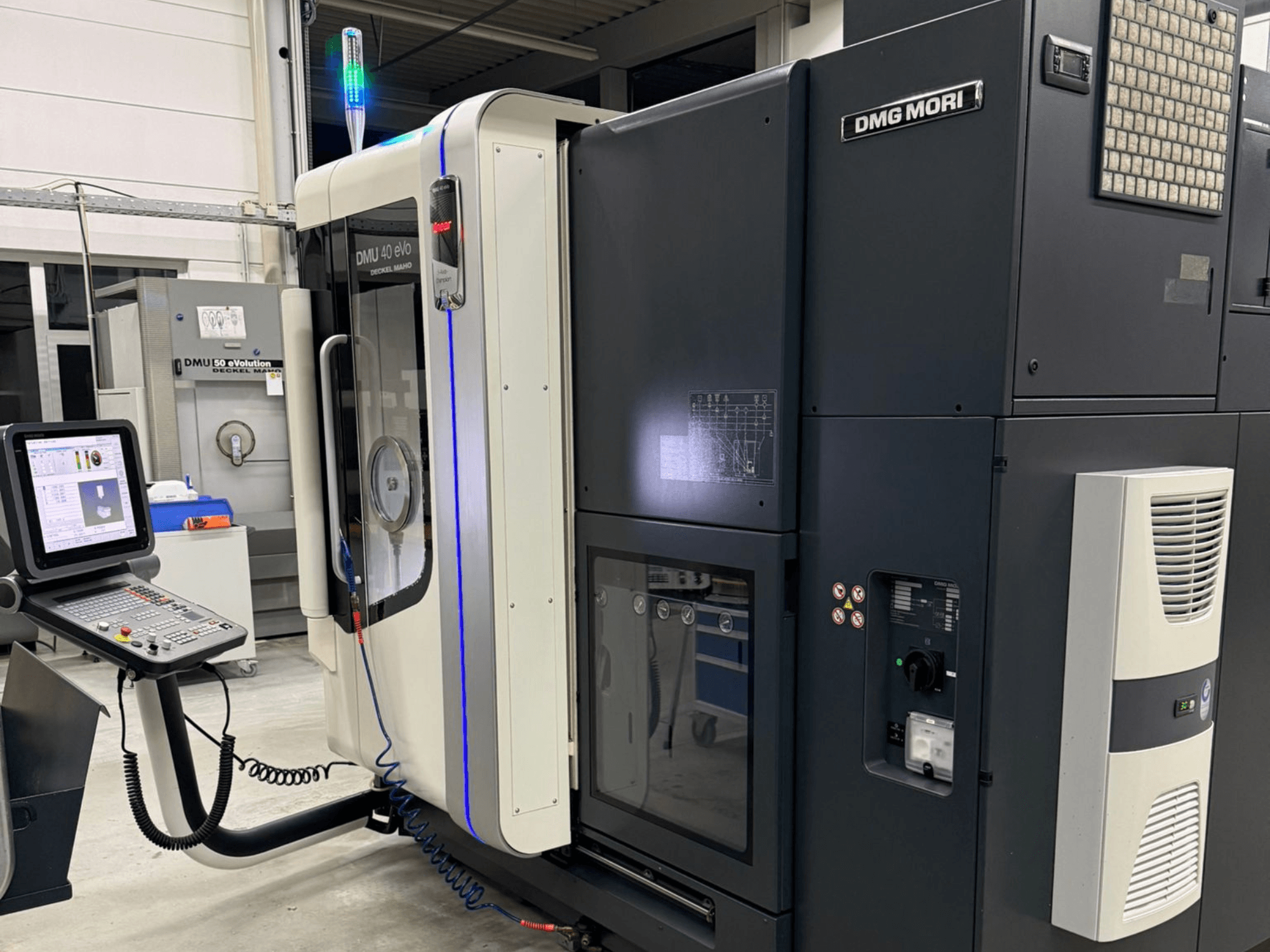 DMG MORI DMU 40 eVo mašīna, priekšējais skats, kurā redzamas vadības ierīces, LED indikatori un glīts dizains, kas izceļ rūpnieciskās iezīmes.