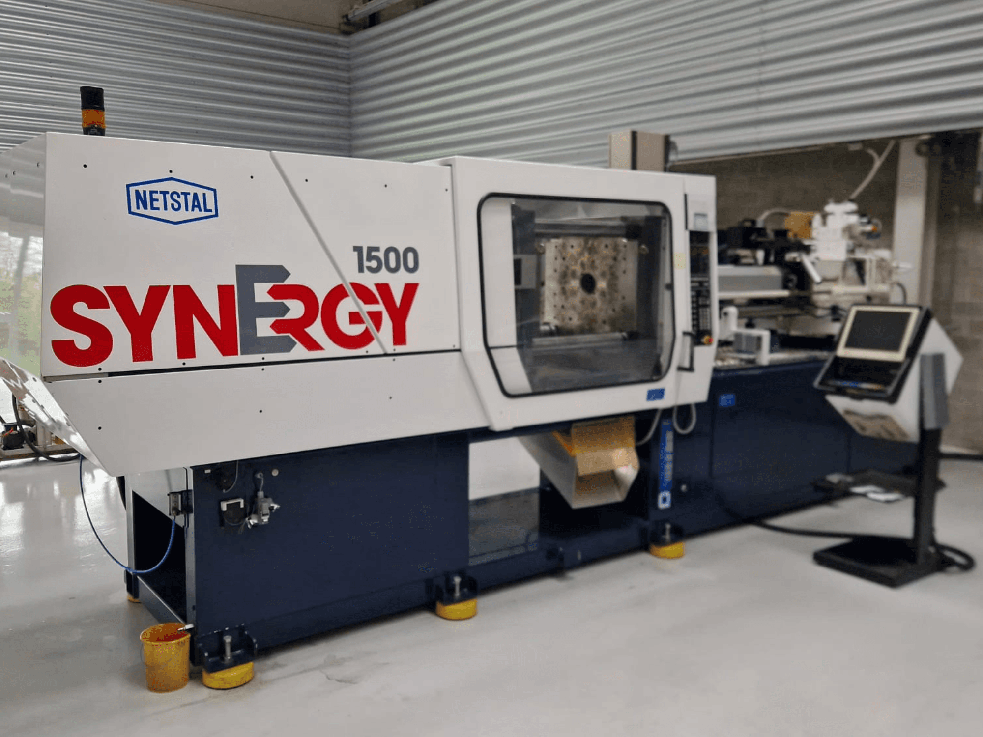 Netstal Synergy 1500-460 hidrauliskā iesmidzināšanas iekārta, skats no priekšpuses, kurā redzams vadības panelis un atvērtā iesmidzināšanas zona.