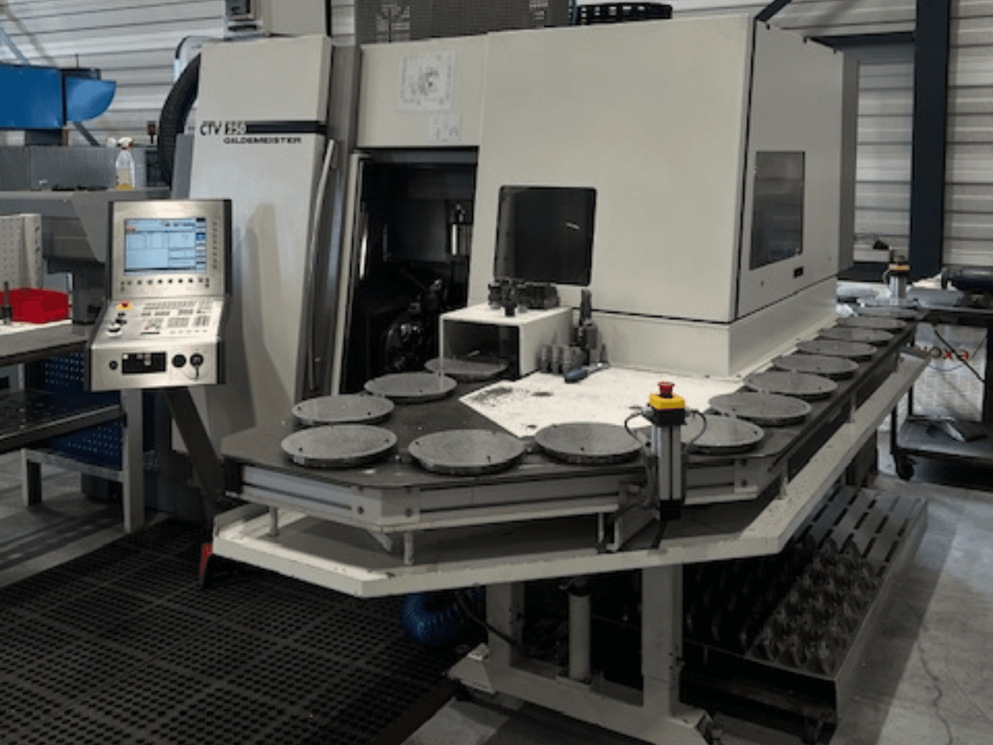 Alt teksts: CTV E33 Goldmeister apstrādes iekārta darbnīcā, skats no priekšpuses, ar vadības paneli un vairākām apļveida darba platformām.