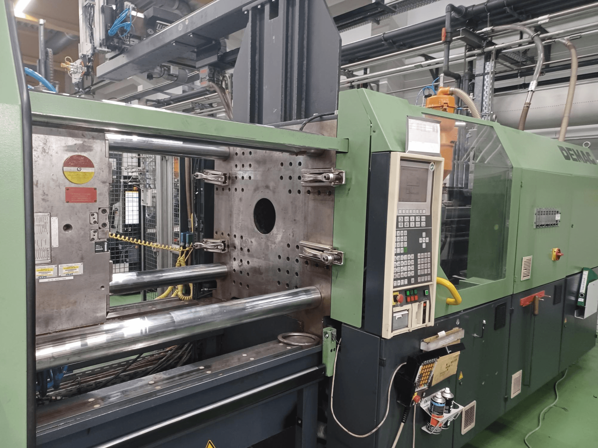 Demag iesmidzināšanas iekārtas priekšējais skats ar vadības paneli, metāla hidrauliskajiem cilindriem un drošības funkcijām.