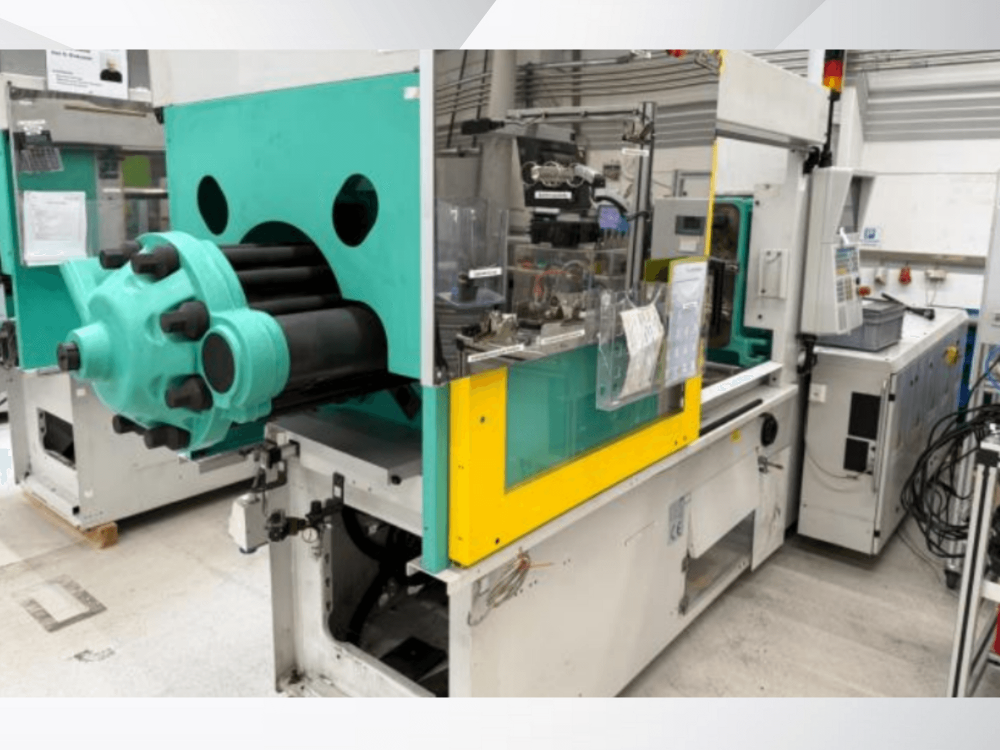 Injekcijas liešanas mašīna, gaiši zilā un dzeltenā krāsā, skats no priekšpuses, ar redzamu veidni un vadības paneli ar uzlīmēm.