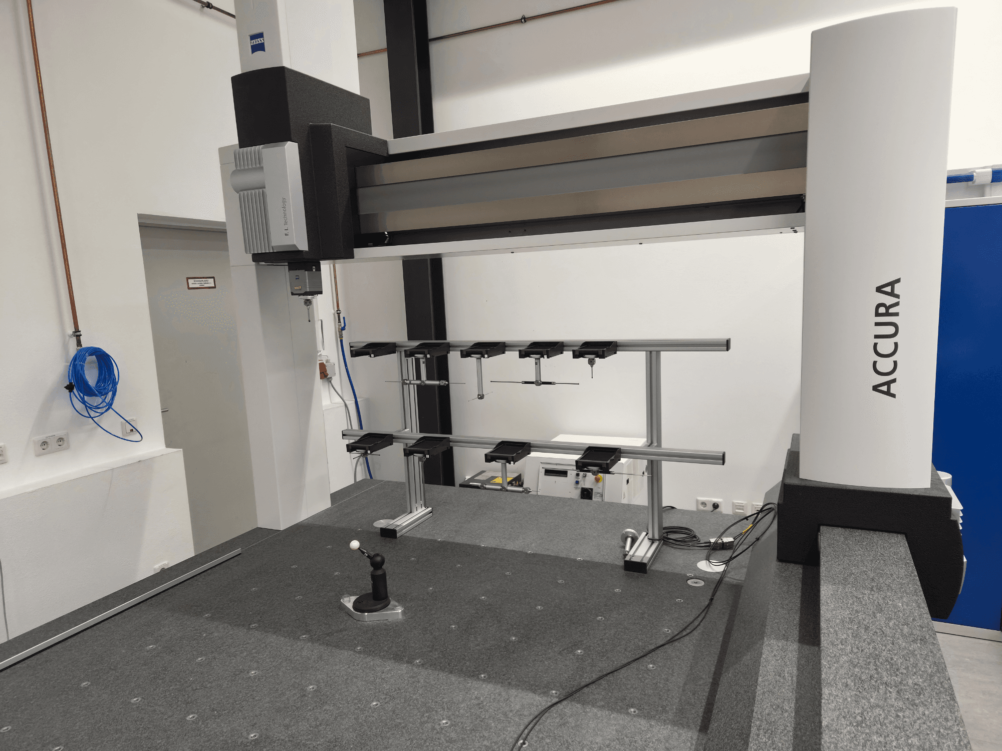 ZEISS ACCURA 16/24/10 CMM skats no priekšpuses, kurā redzams mērīšanas rokturis, pamatne un vadības interfeiss uz pelēkas paklājas virsmas.
