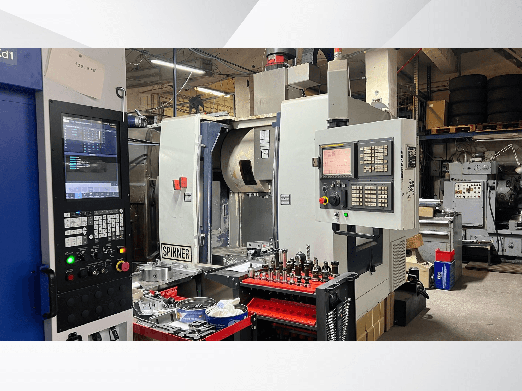 CNC darbagalds ar vadības paneli, instrumentiem un apstrādājamām detaļām, skatoties no priekšējā leņķa darbnīcas vidē.
