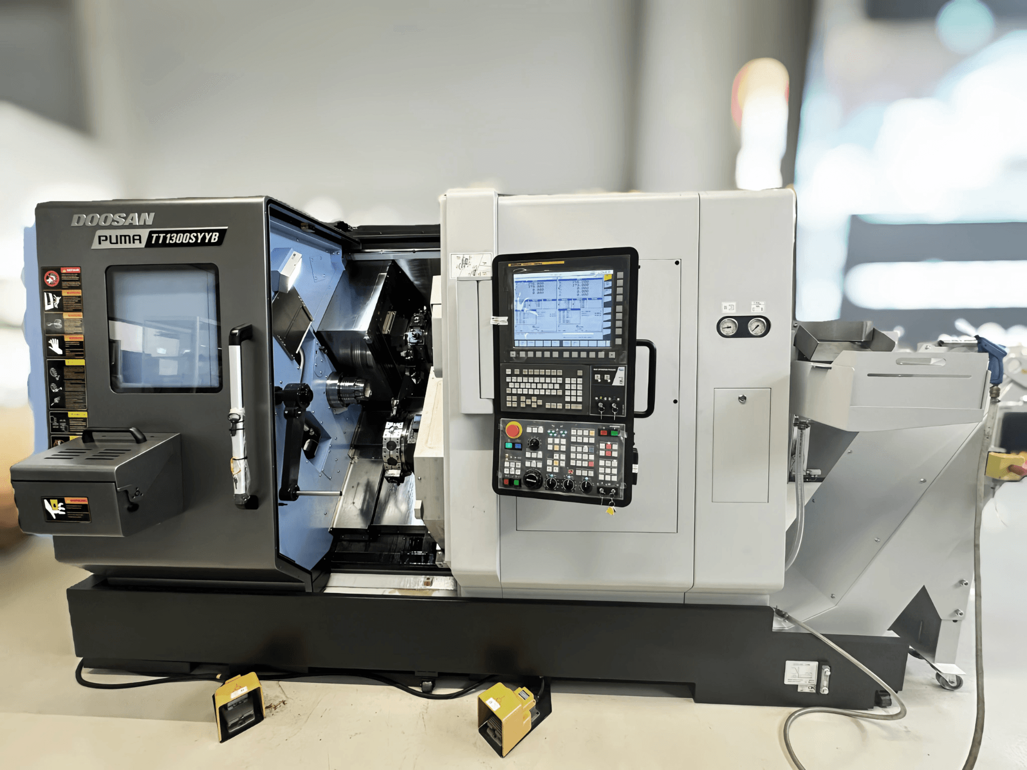 Doosan Puma TT1300SYYB rotācijas frēzēšanas centrs sānu skatā, redzams vadības panelis un mašīnas iekšpuse ar redzamiem instrumentiem.