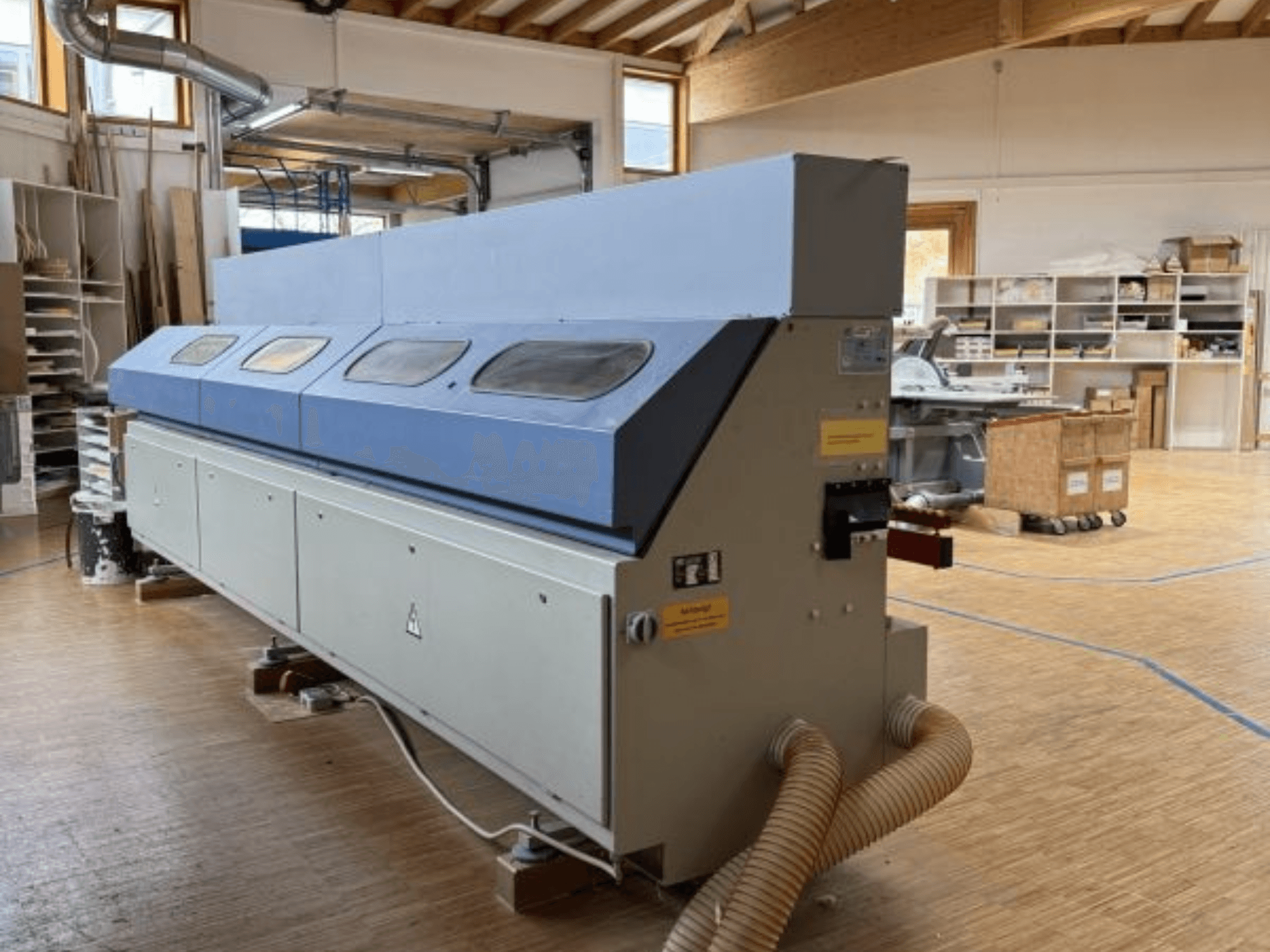 OTT Pacific V6-F malu slīpmašīna parādīta no sānu skata; ar garu zilu augšējo daļu un vadības paneli ar šļūtenes stiprinājumu.