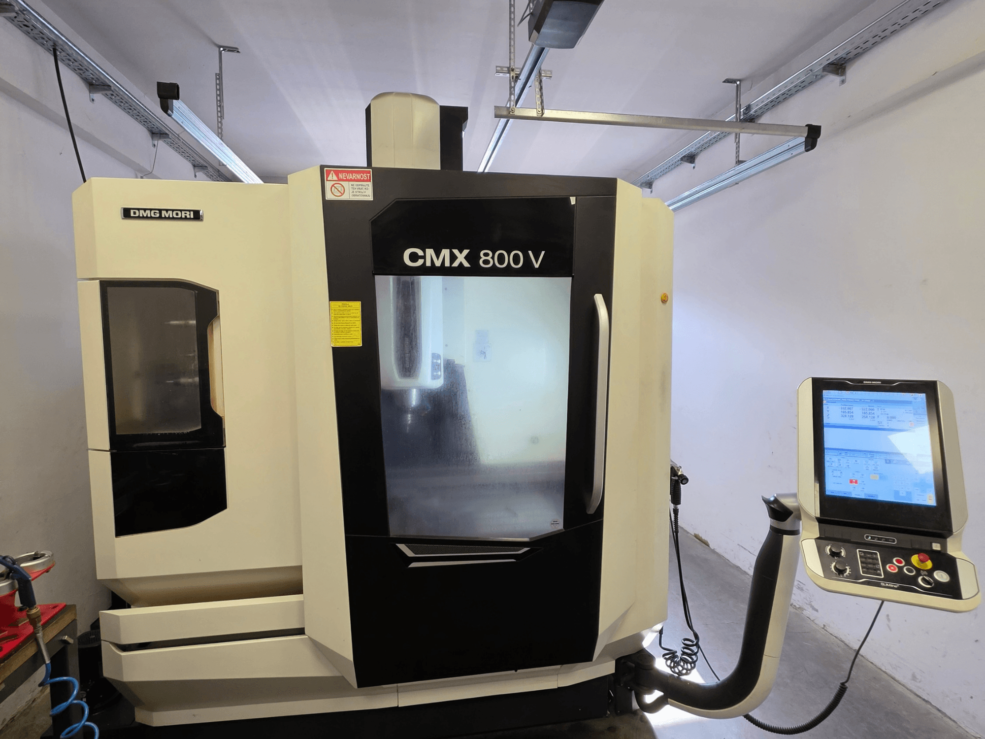 Vertikālais apstrādes centrs DMG MORI CMX 800V, skats no priekšpuses, ar skārienjūtīgo vadības paneli un skaidriem drošības norādījumiem.