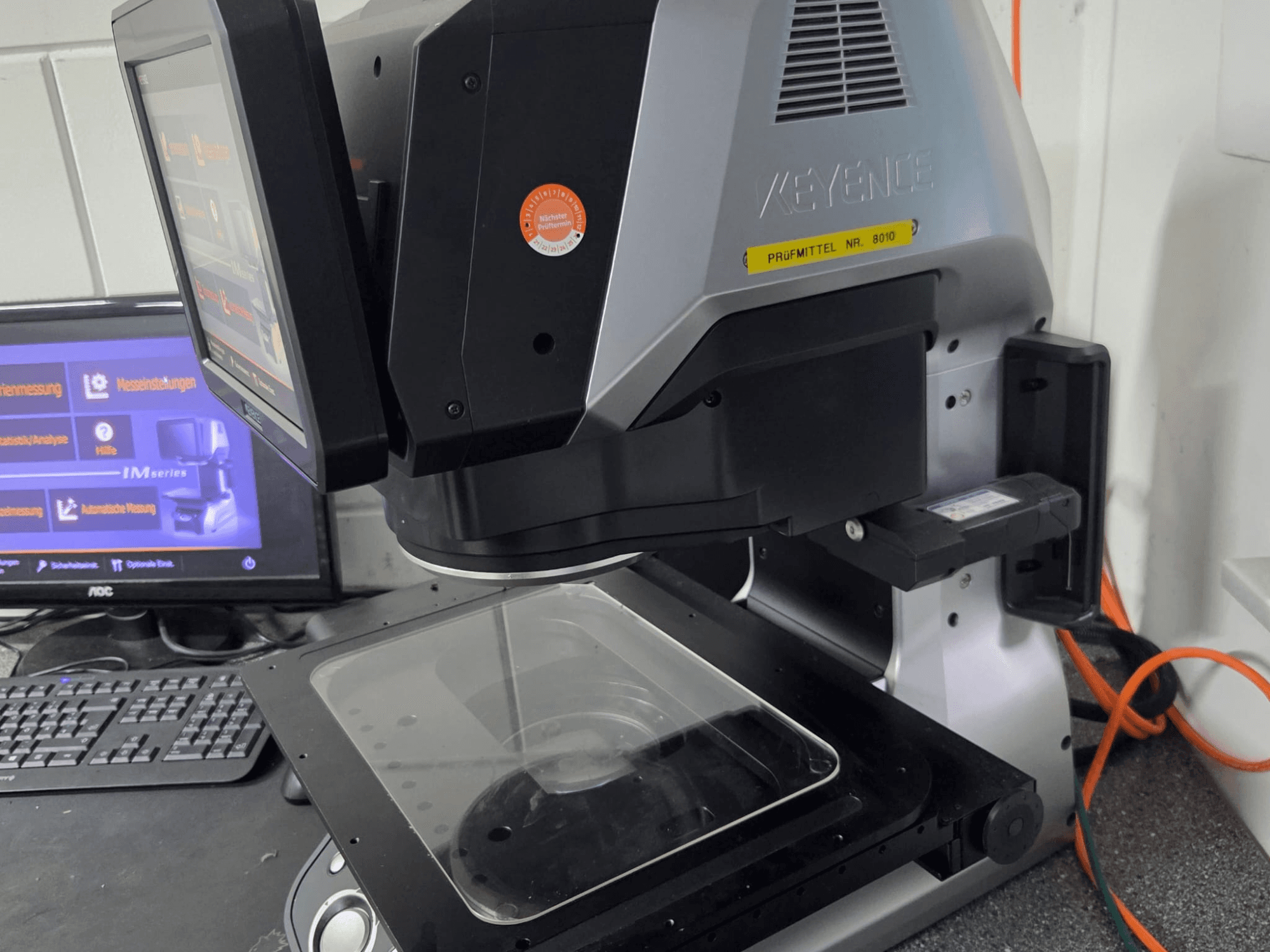 KEYENCE IM 7030 optiskā mērīšanas iekārta, priekšējais skats ar skārienjūtīgo ekrānu un stikla mērījumu plāksni.