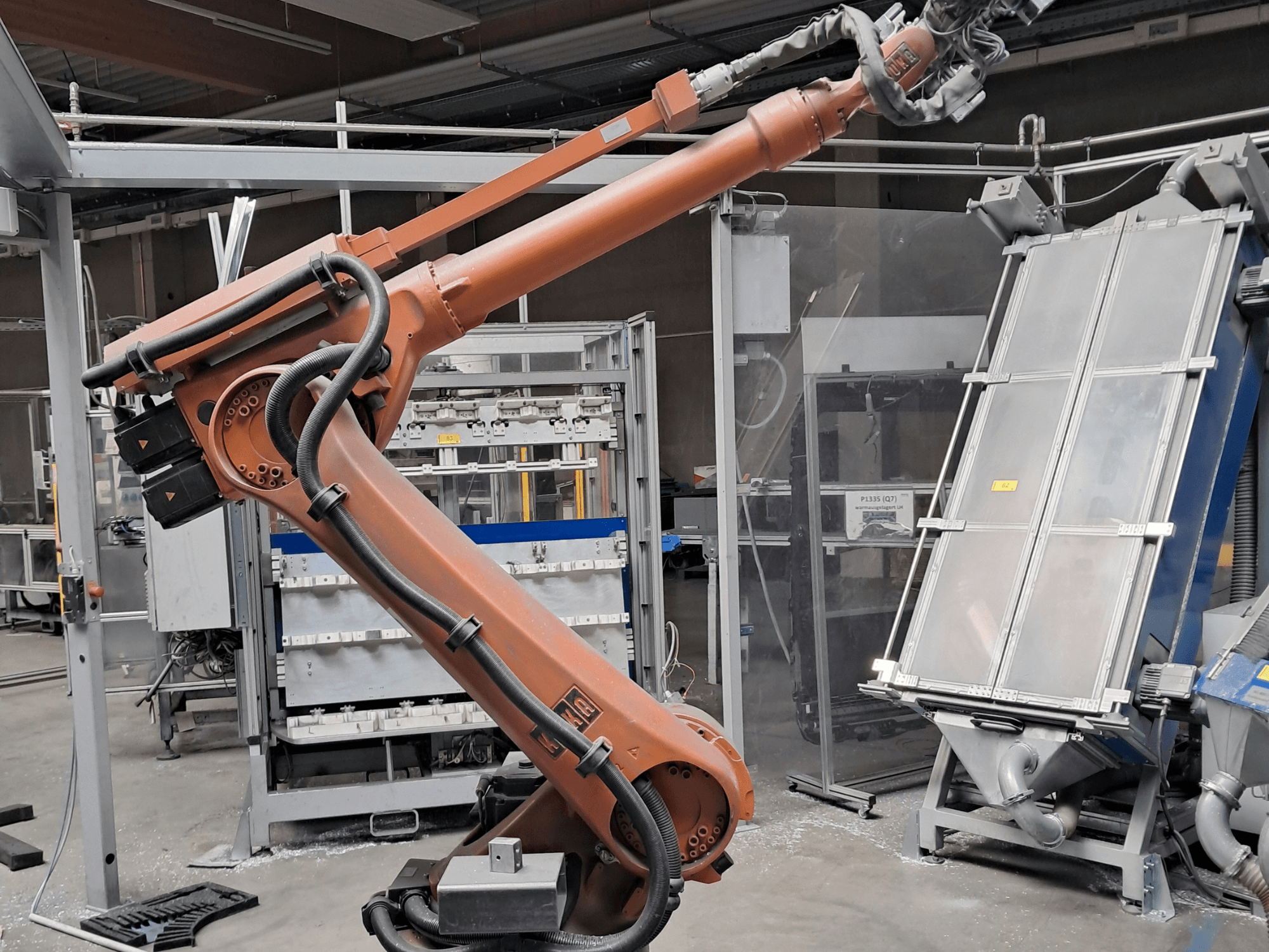 KUKA KR 30L16-2 robota roka rūpnīcas vidē, sānskats, kurā redzami kabeļi un mehāniskās detaļas.