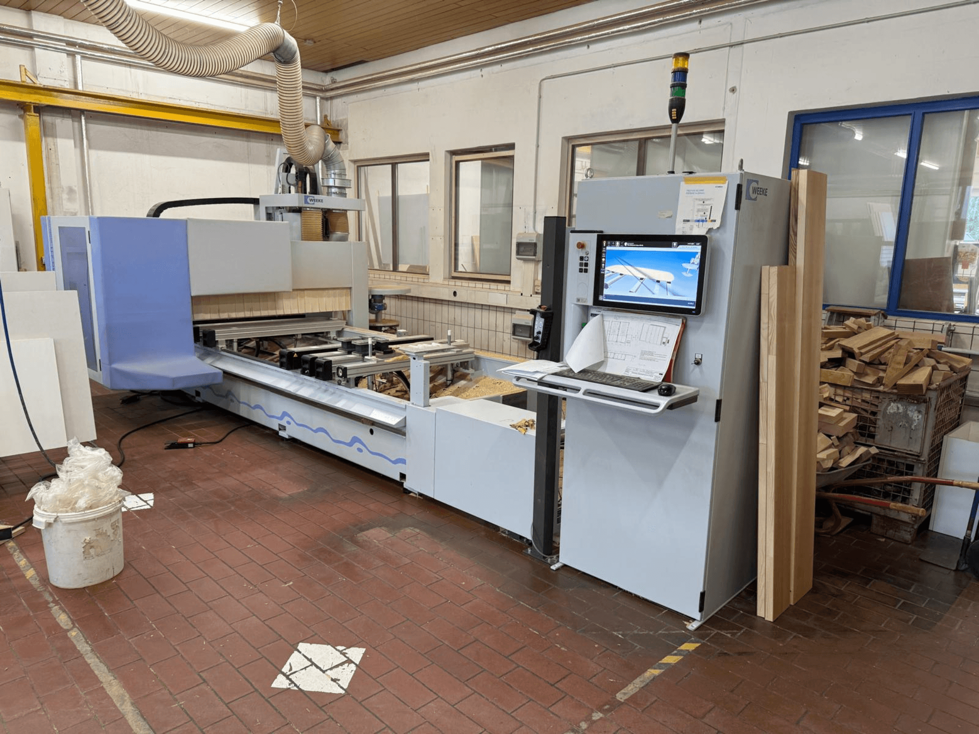 Weeke PROFI BMG211/32/12/K CNC koka apstrādes centrs, skats no priekšpuses, redzams vadības panelis un koka gabali, aprīkots ar putekļu nosūces sistēmu.